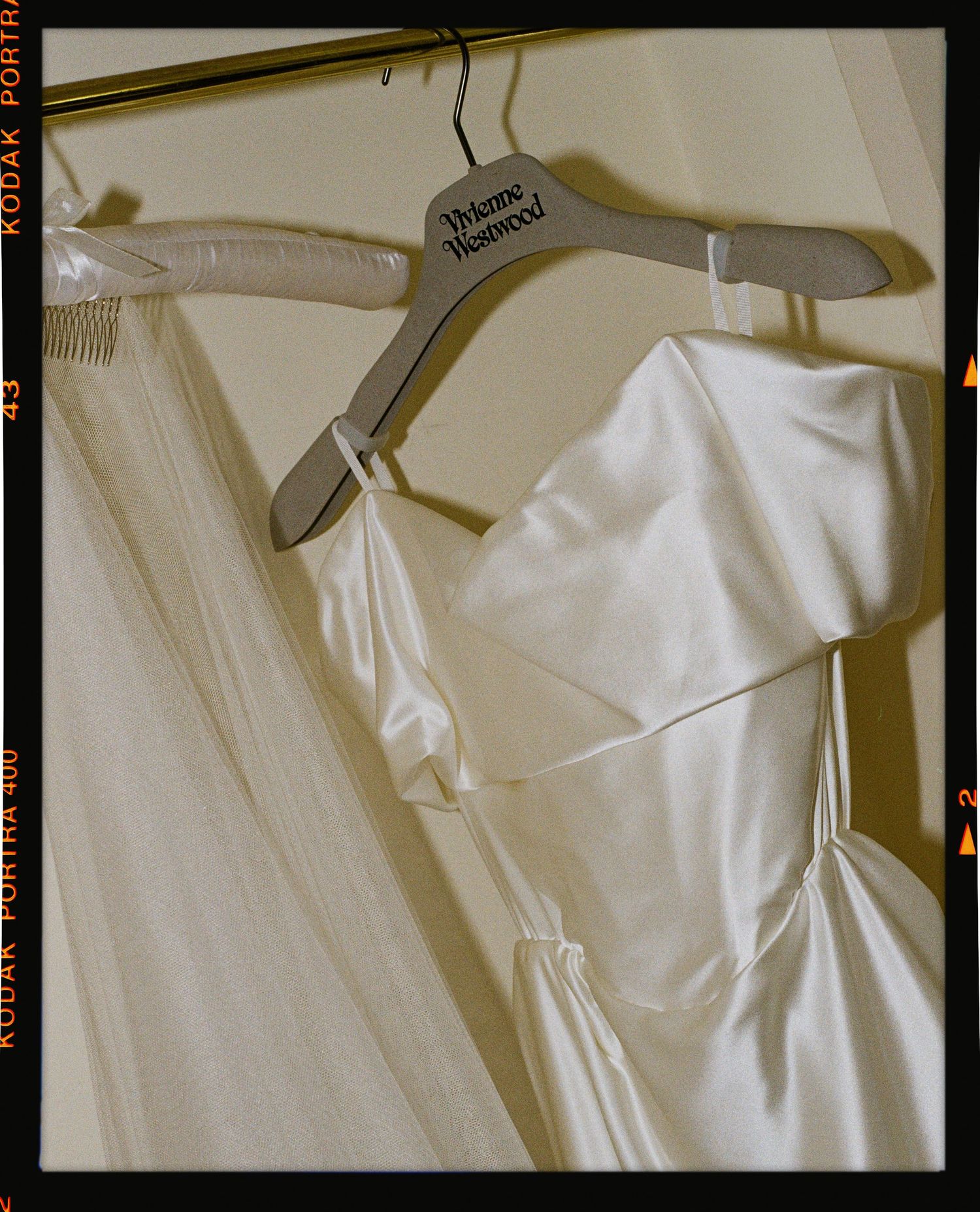 White satin slip dress on a Vivienne Westwood hanger, displayed on a clothing rack with sheer fabric.