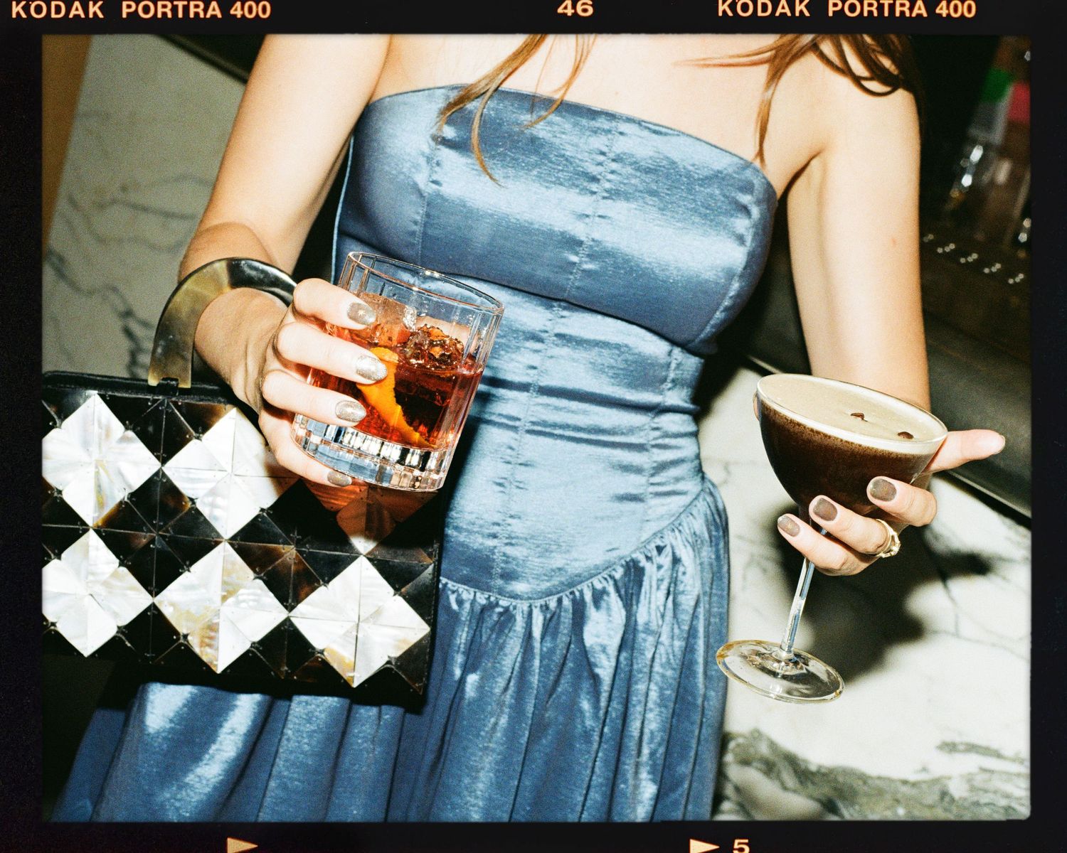 Woman in blue strapless dress holding cocktails at a party, shot on Kodak Portra 400 film.