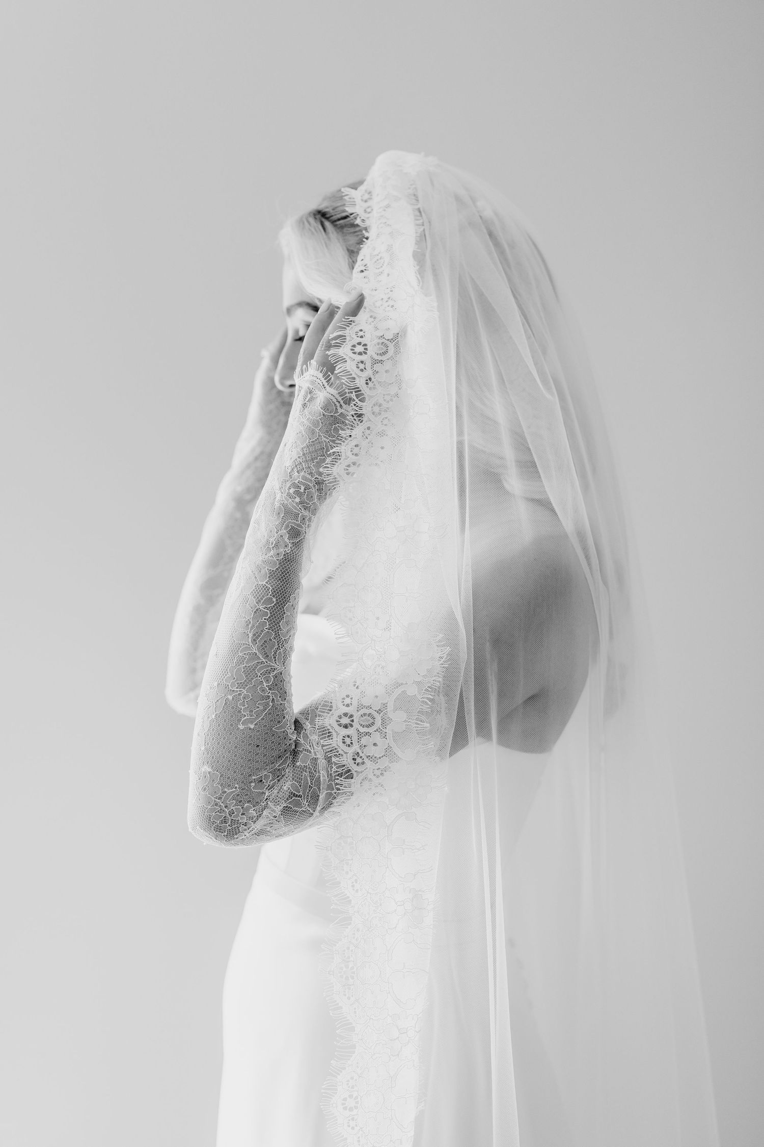 Black and white photo of a bride in lace wedding dress and veil, elegant side profile portrait.