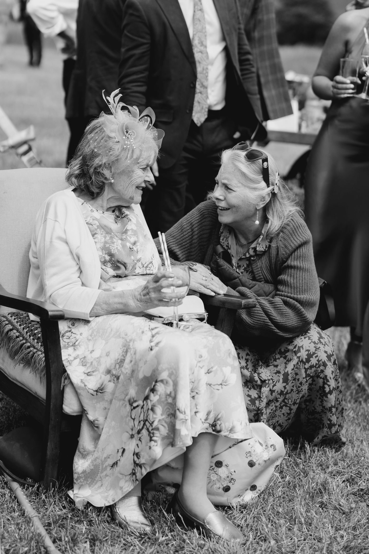 Two elderly women share a joyful conversation at an outdoor wedding reception in black and white photo.