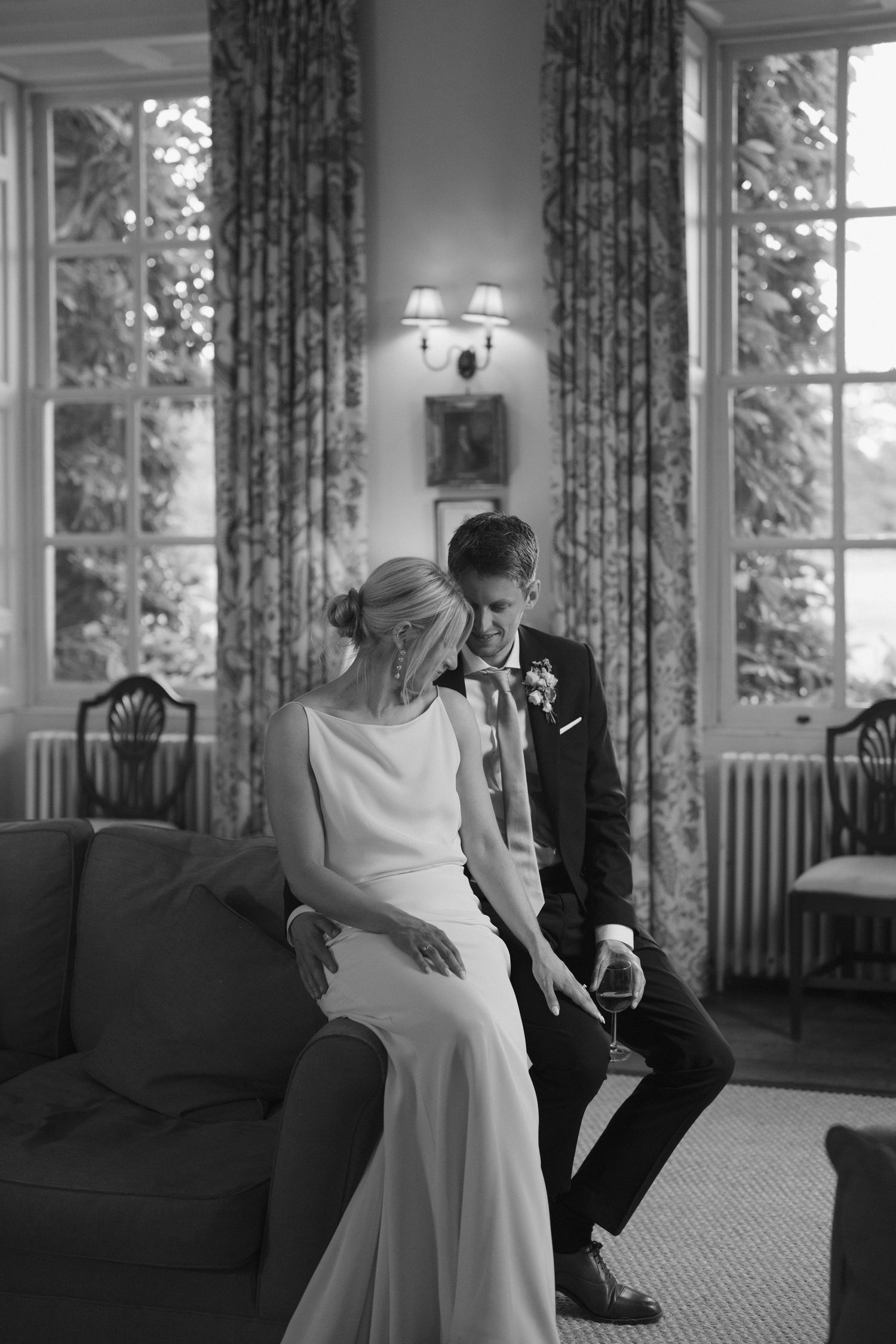 Black and white photo of bride and groom sharing intimate moment on sofa in elegant room.