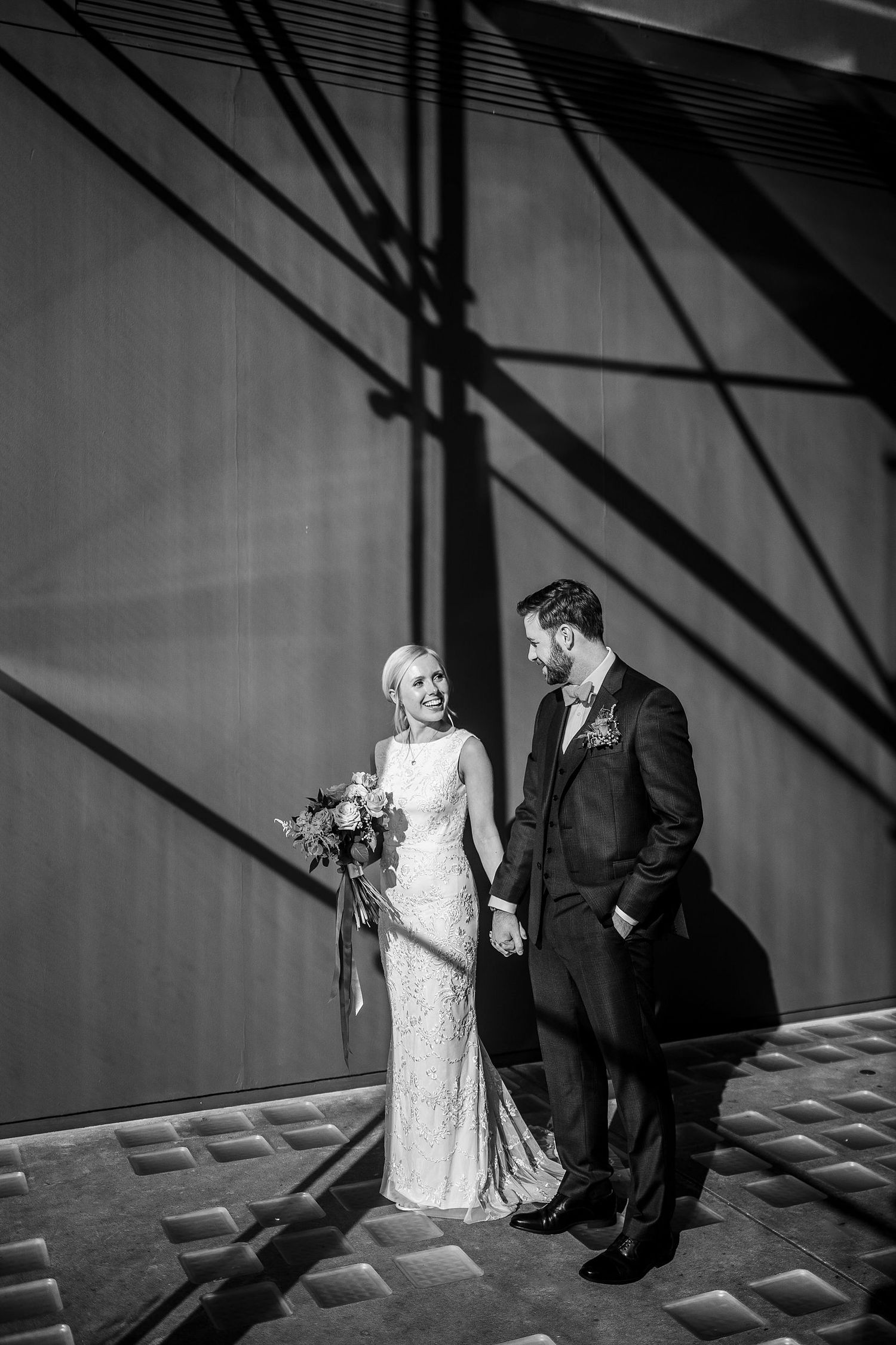 Bride and groom sharing romantic moment beside bold geometric shadows in black and white.