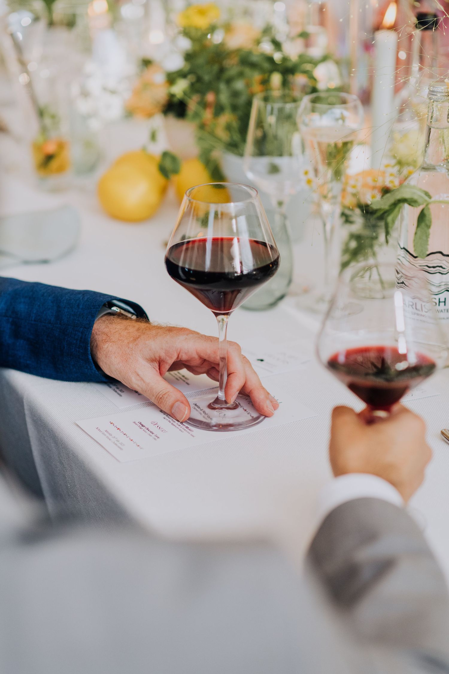 Close-up of hands holding red wine glasses over a white tablecloth with a wedding menu card.