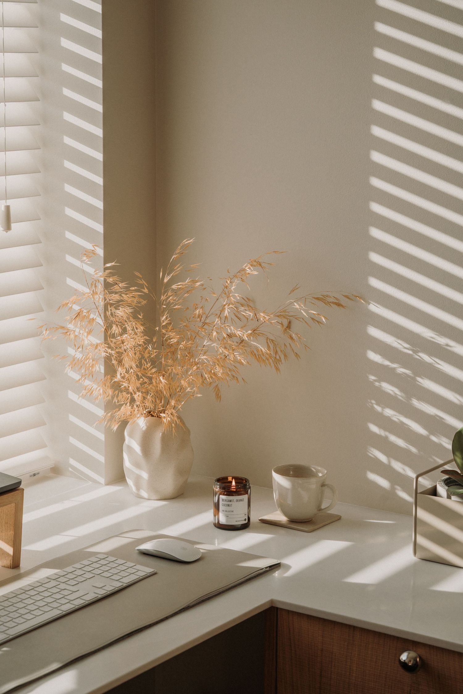 Minimalist home desk with dried pampas grass, candle, and coffee cup bathed in window light.