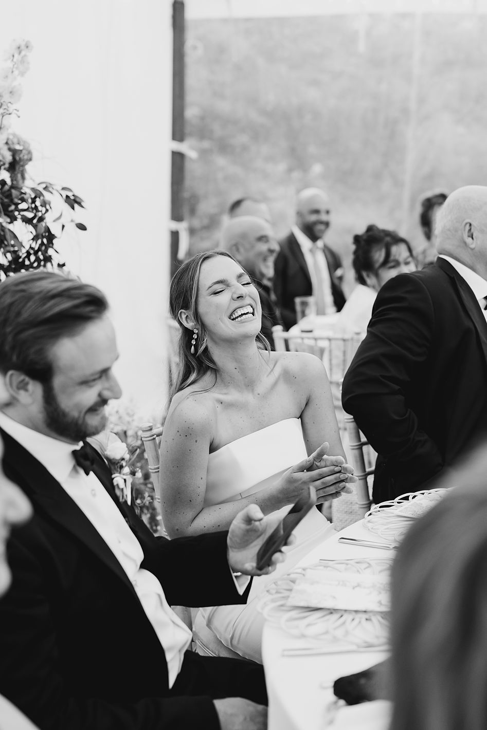 Black and white photo of laughing bride in strapless gown at elegant outdoor wedding reception.