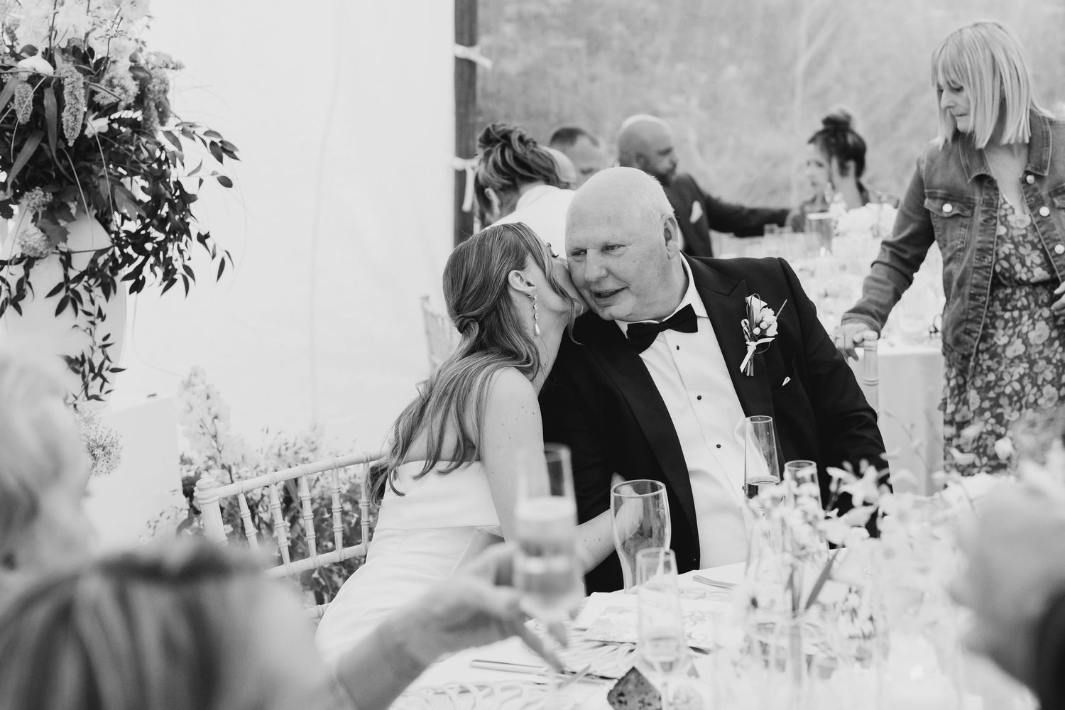 Black and white photo of bride and groom sharing intimate moment at wedding reception dinner table.
