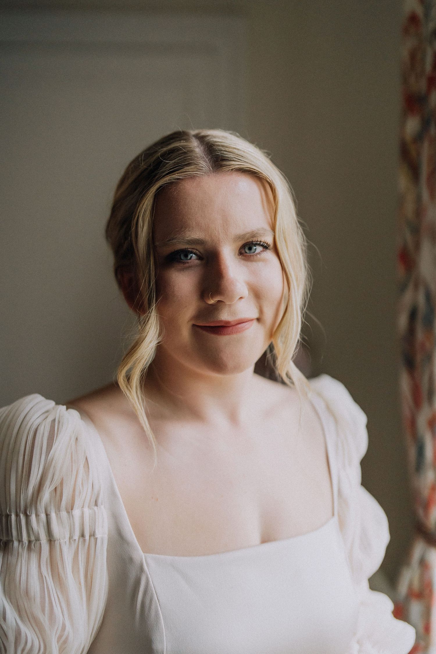 Portrait of smiling blonde bride in white square-neck puff sleeve wedding dress indoors.