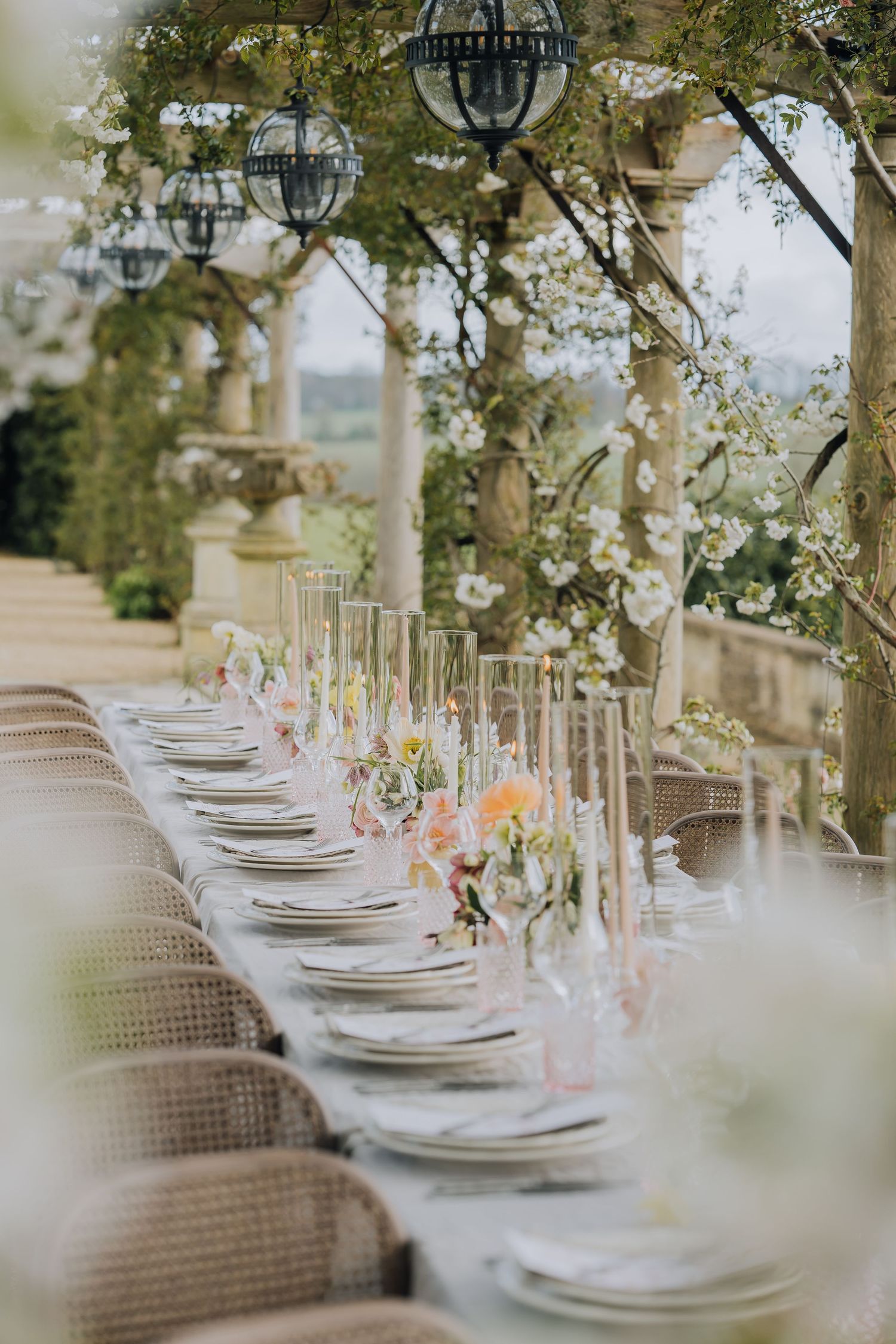 Elegant outdoor wedding reception long table with floral centerpieces under a stone pergola.
