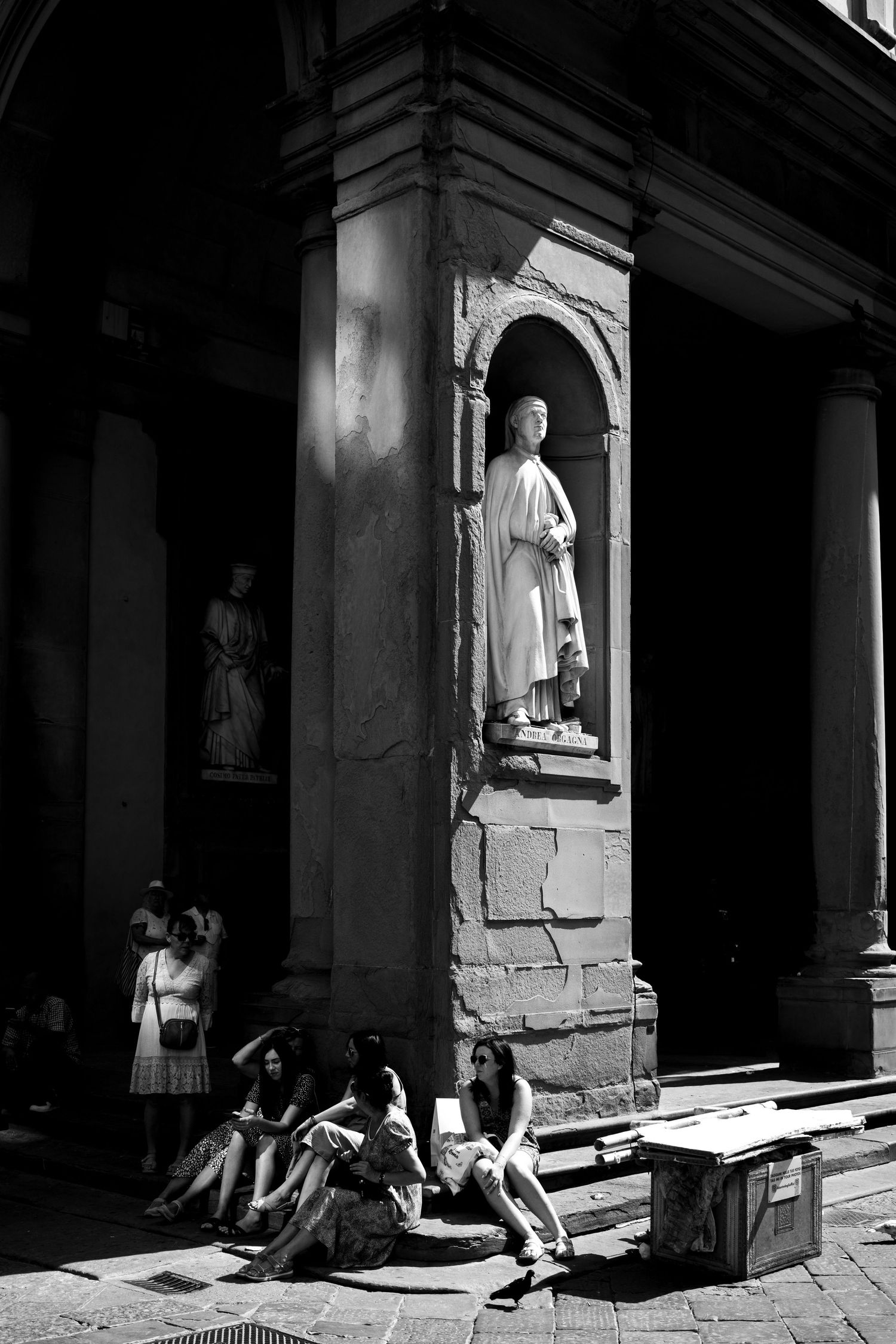 People sitting at the base of a classical statue in a historic Italian building in black and white.