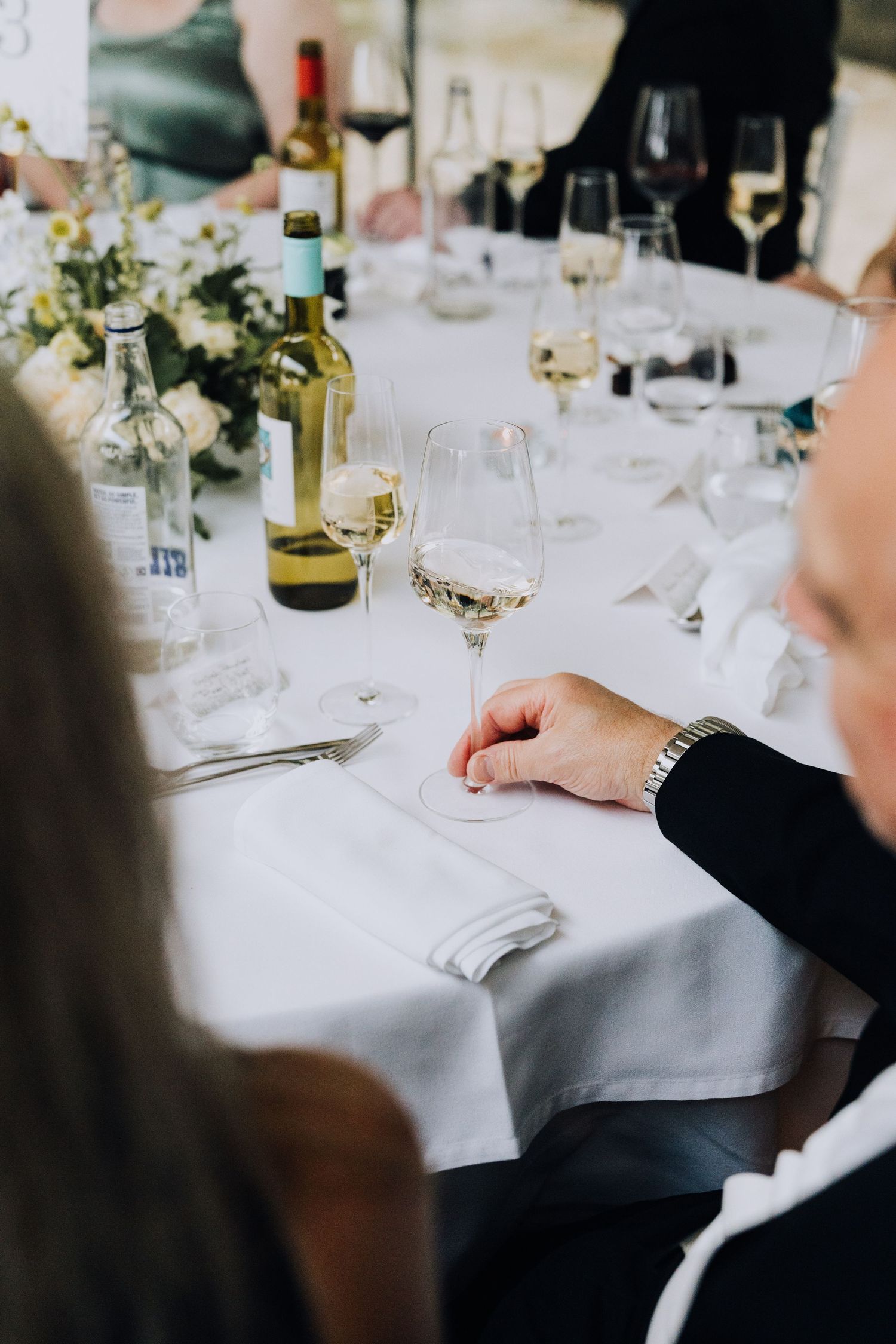 Wedding reception table with white linen, wine glasses, and bottles of white wine.