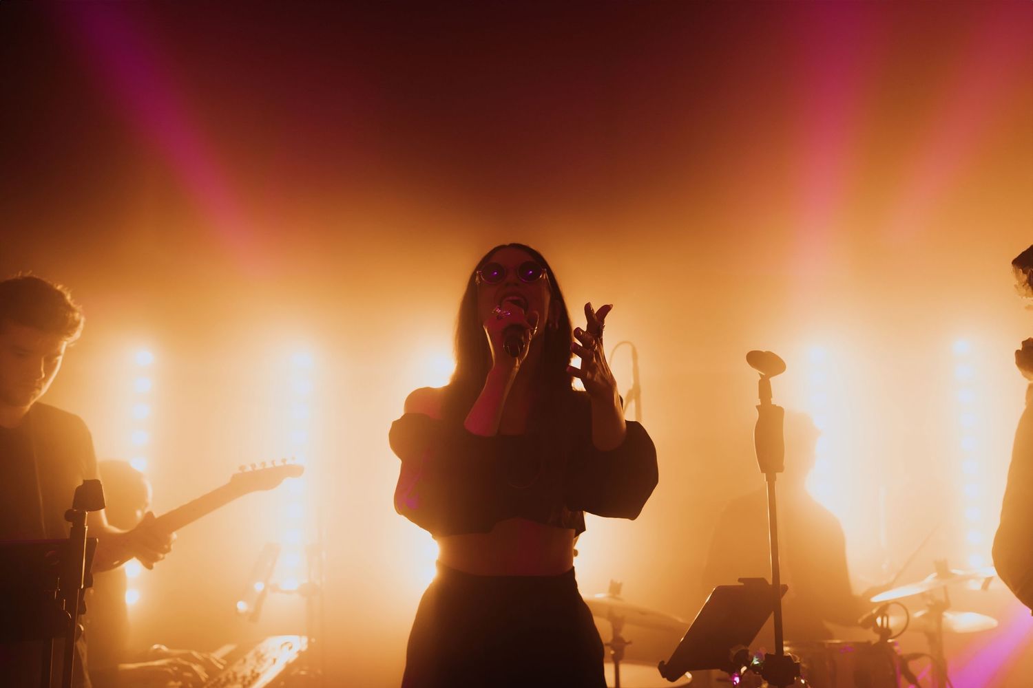 Female wedding singer performing on dramatic stage with warm golden spotlights and band members behind her.