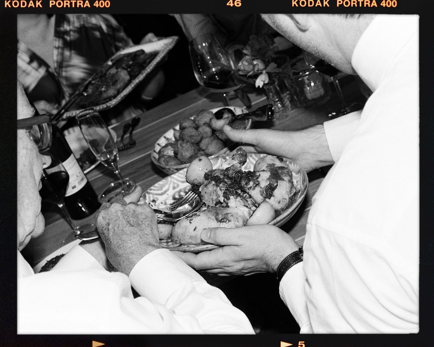 Black and white film photo of hands holding a plate of food at a dinner gathering on Kodak Portra 400. Taken at Dorfold Hall