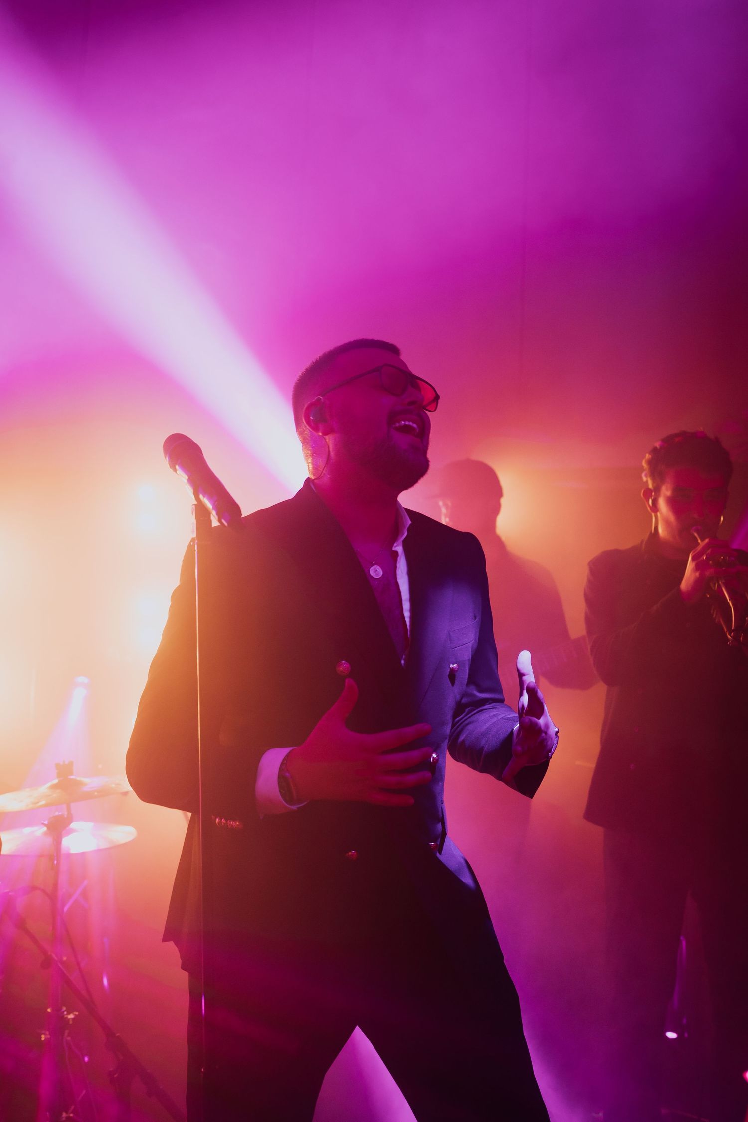 A passionate male singer performs on stage bathed in vibrant purple and orange lights at a wedding reception.