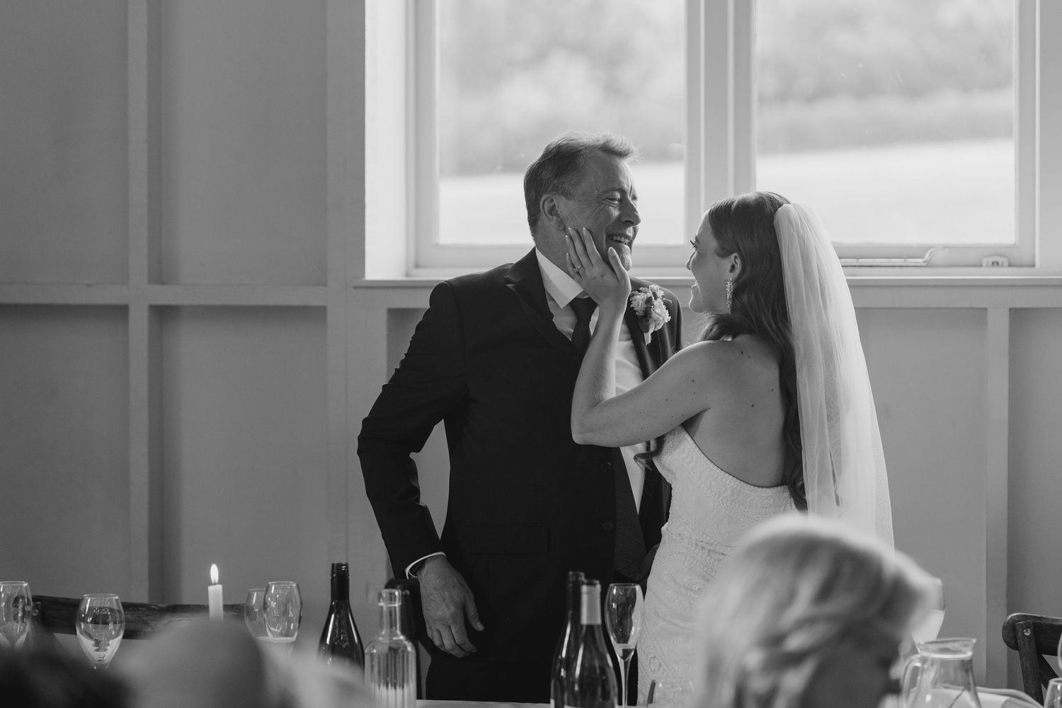 Emotional black and white photo of bride tenderly touching grooms face during wedding reception speeches.