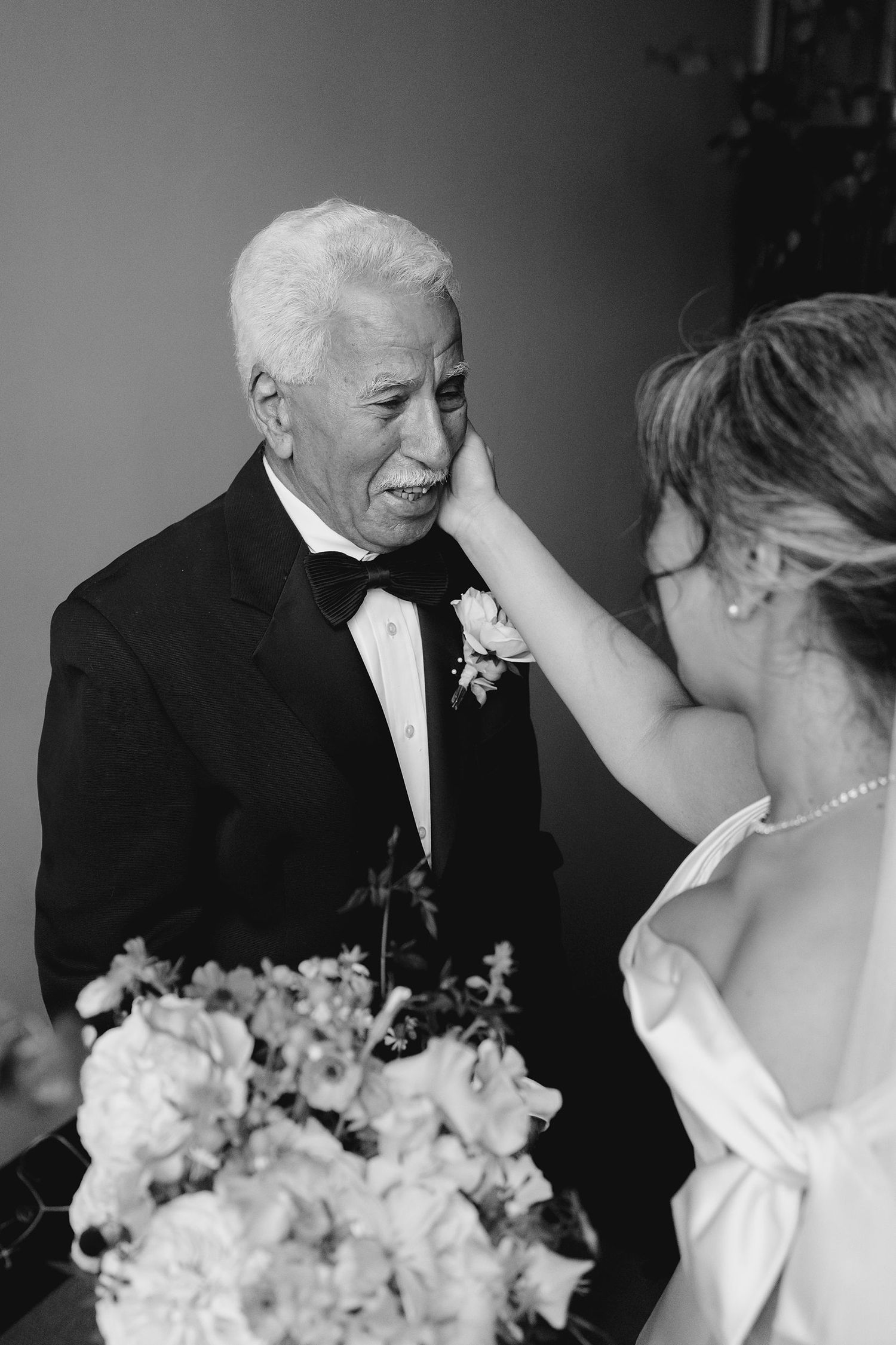 Emotional black and white moment of bride wiping tears from elderly mans cheek at wedding.