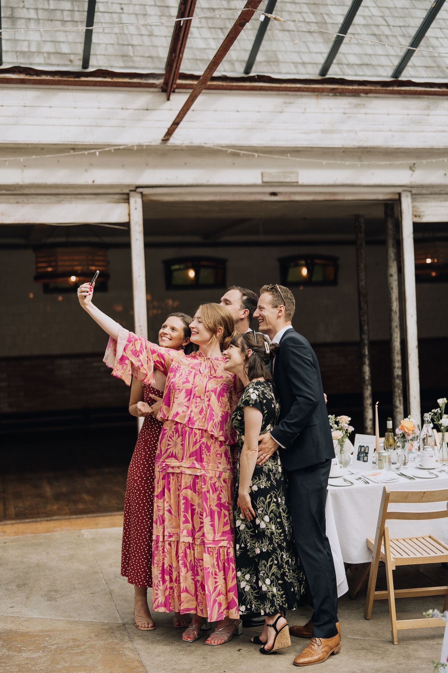 Group of wedding guests in colorful dresses taking a selfie at an outdoor barn wedding venue.