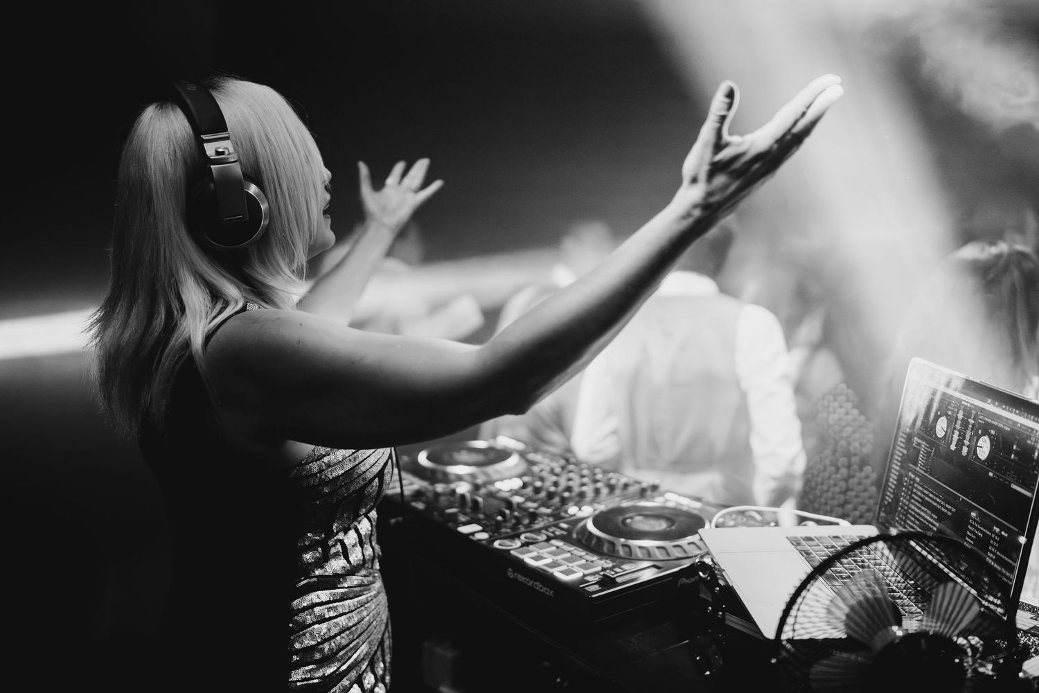 Black and white photo of a female DJ with headphones performing at a wedding reception party.