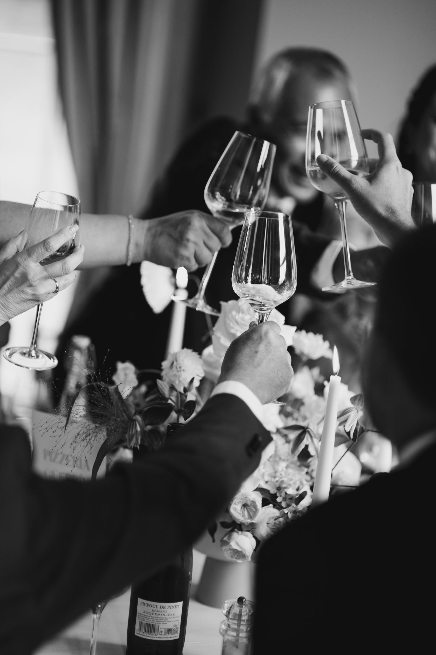 Wedding guests clinking wine glasses in celebratory toast over floral centerpiece at reception dinner table.
