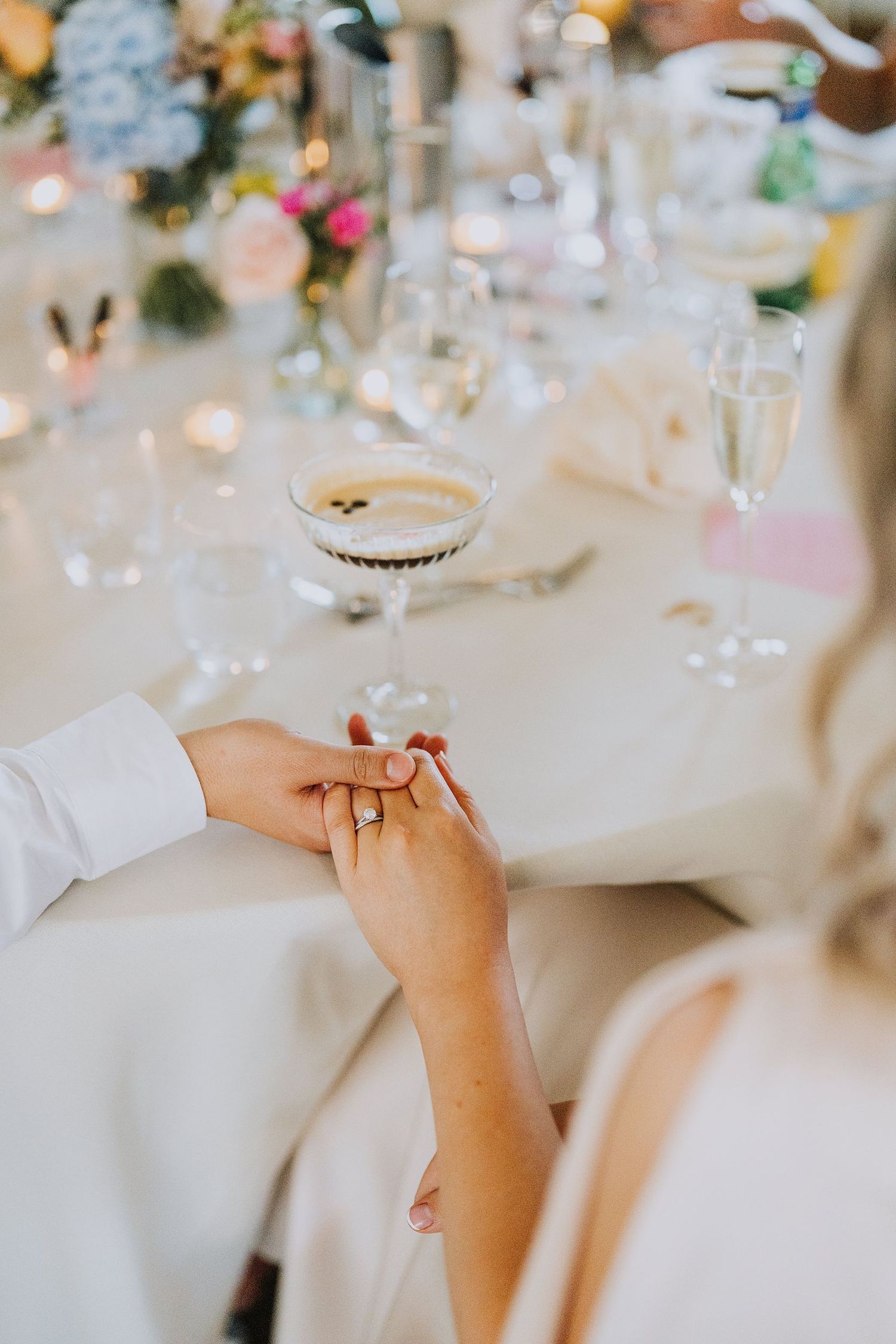 Bride and groom holding hands at elegant wedding reception table with champagne flutes and floral centerpieces.