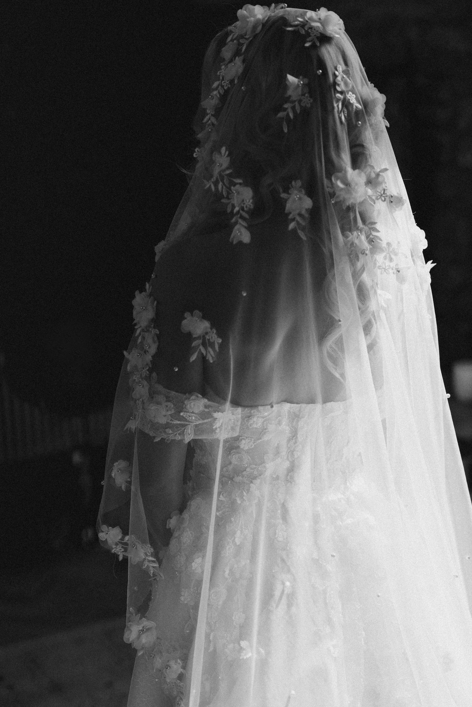 Elegant bride photographed from behind wearing a floral lace cathedral veil in black and white.