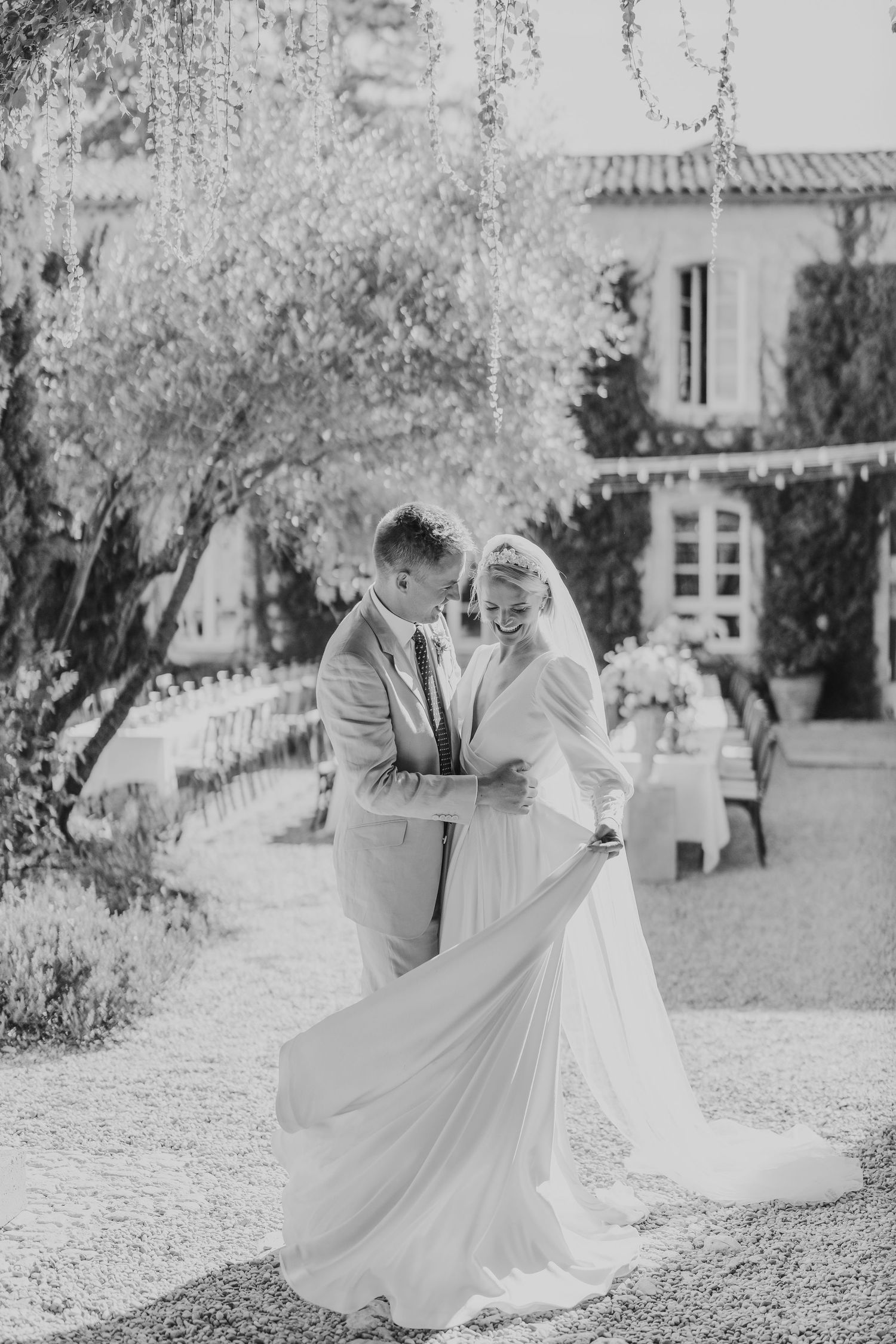 Black and white photo of bride and groom dancing together in a romantic garden with elegant reception tables behind.