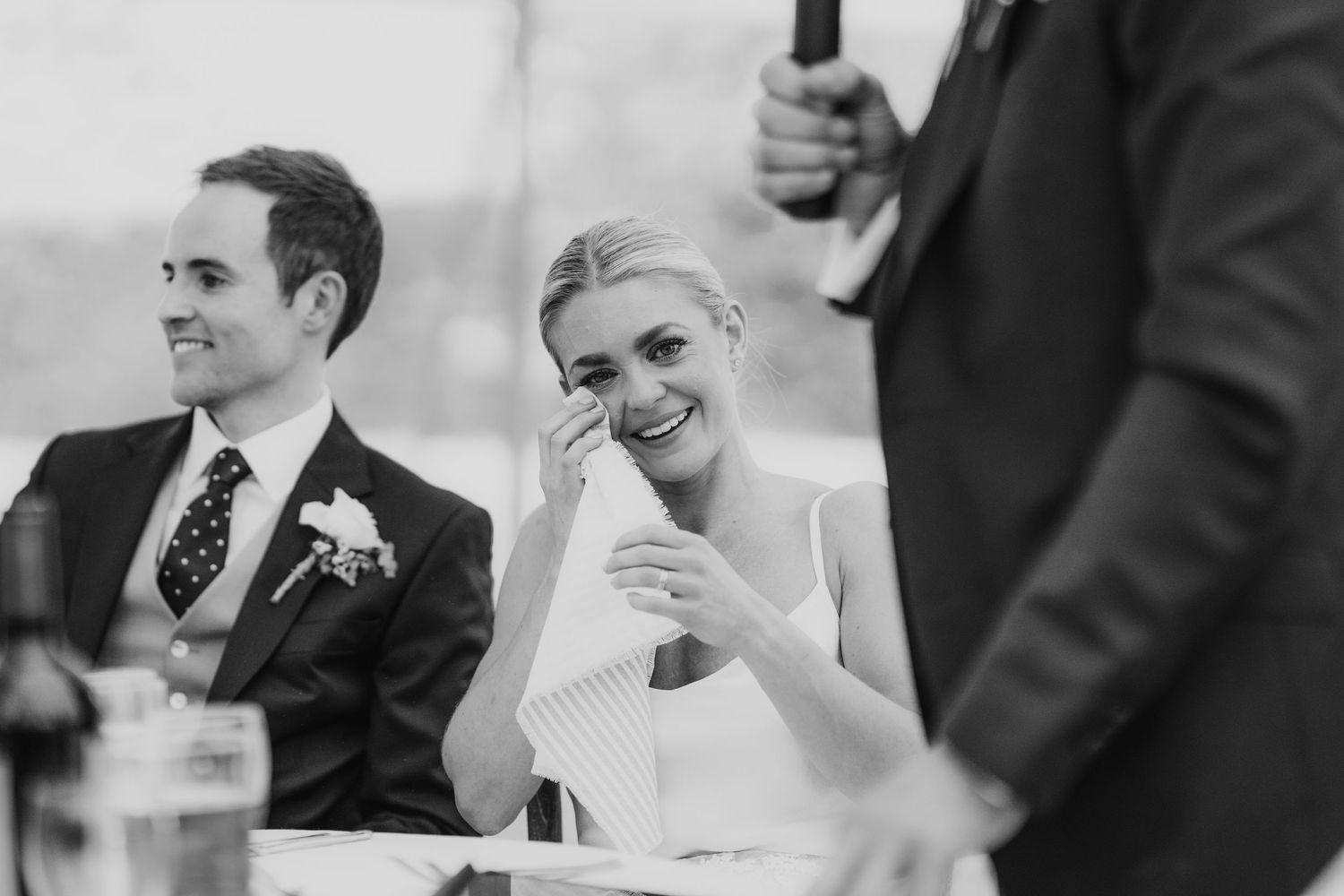 Black and white photo of bride wiping happy tears during heartfelt wedding reception speech.