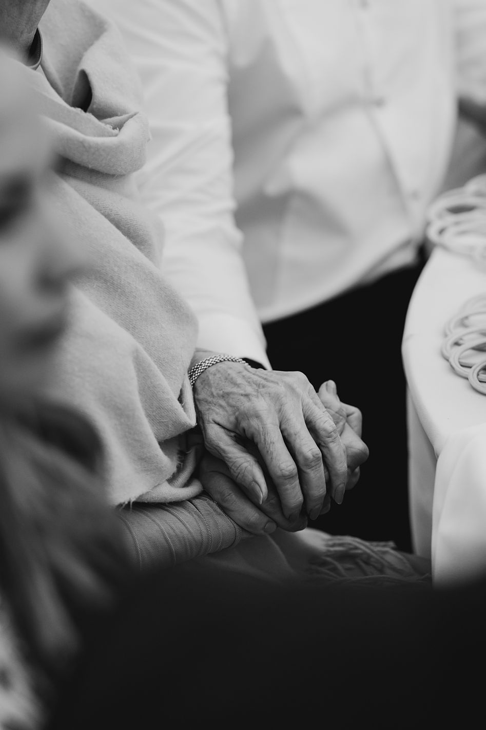 Close-up black and white photo of elderly hands tenderly held together during a wedding ceremony.
