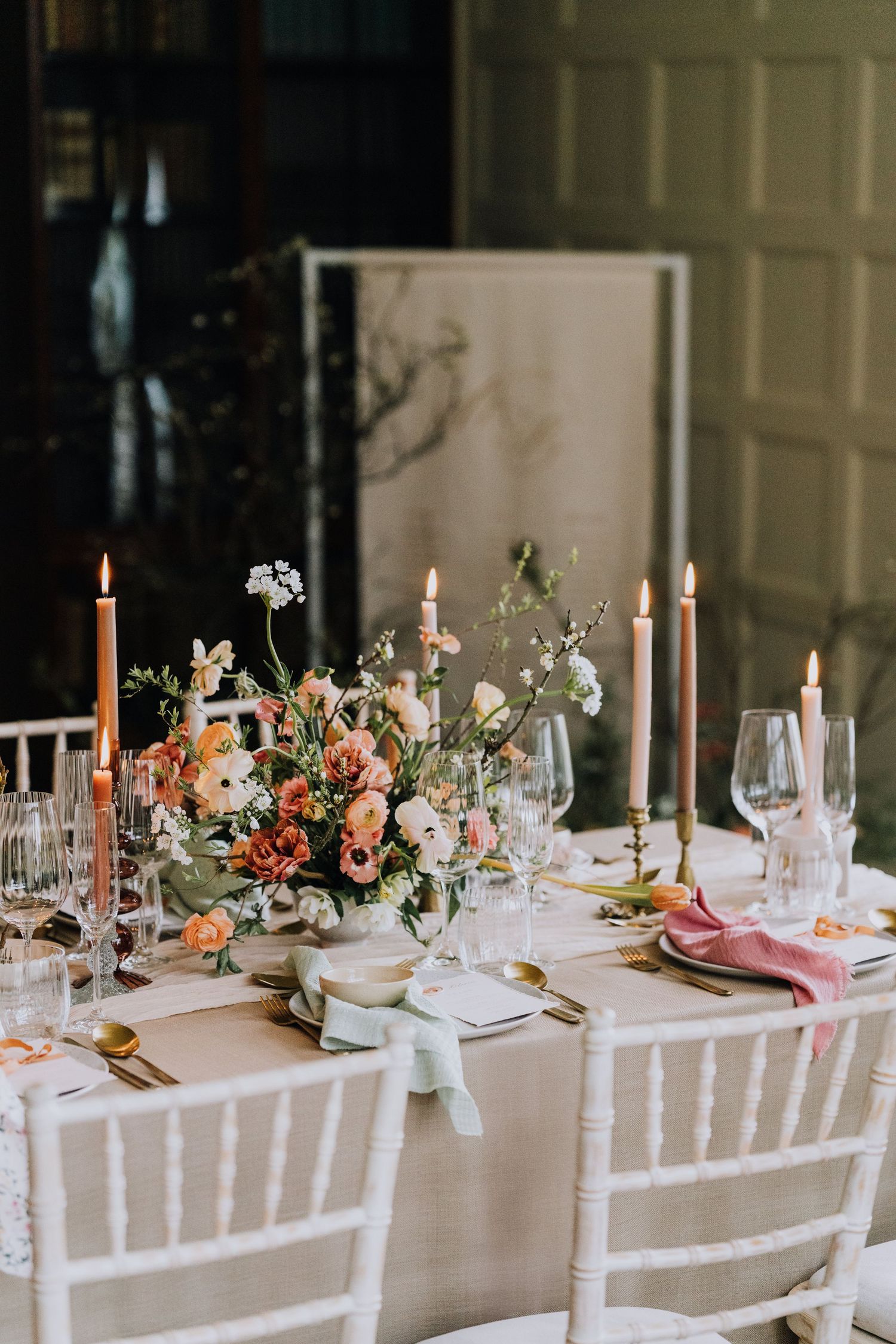 Romantic wedding reception table with peach and pink floral centerpiece, taper candles, and gold cutlery.