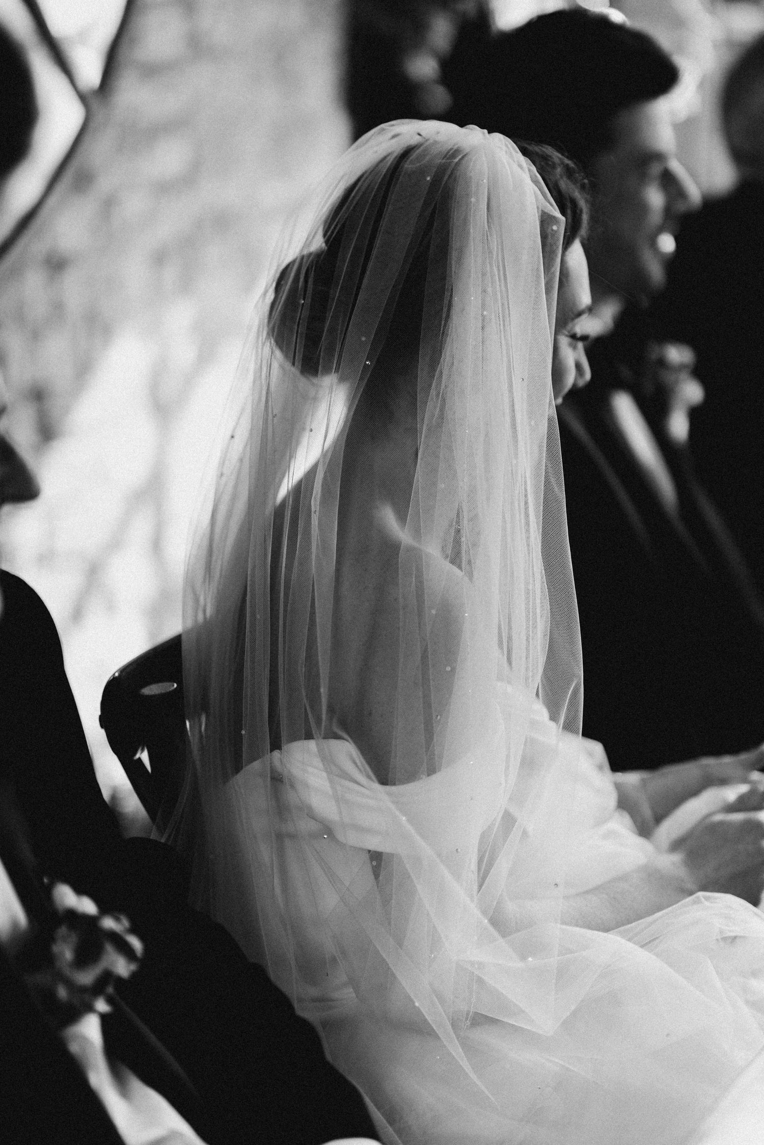 Black and white photo of a bride wearing a delicate veil during a wedding ceremony.