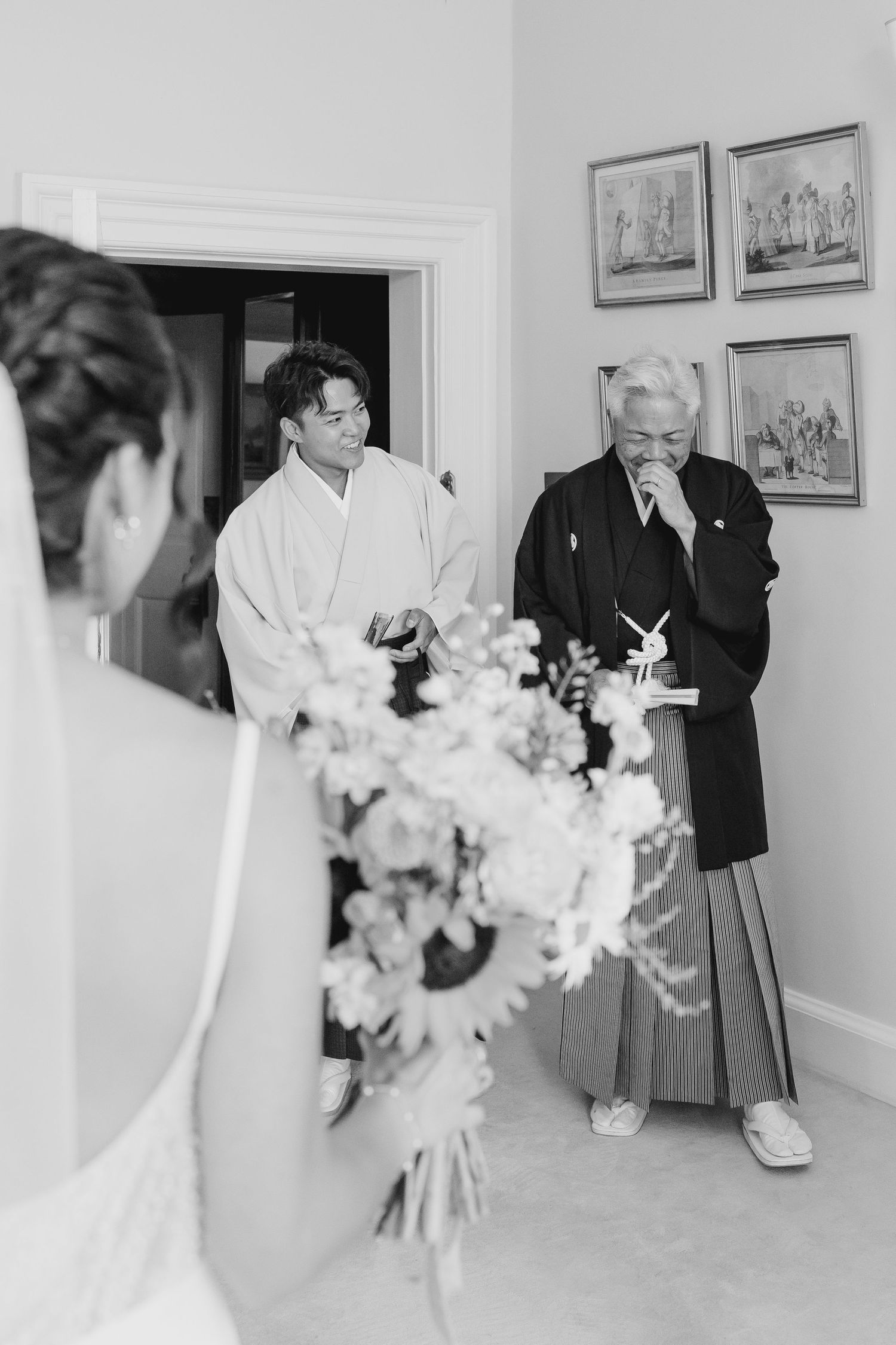 Black and white photo of emotional family members in traditional Japanese attire reacting to a bride holding a floral bouquet.