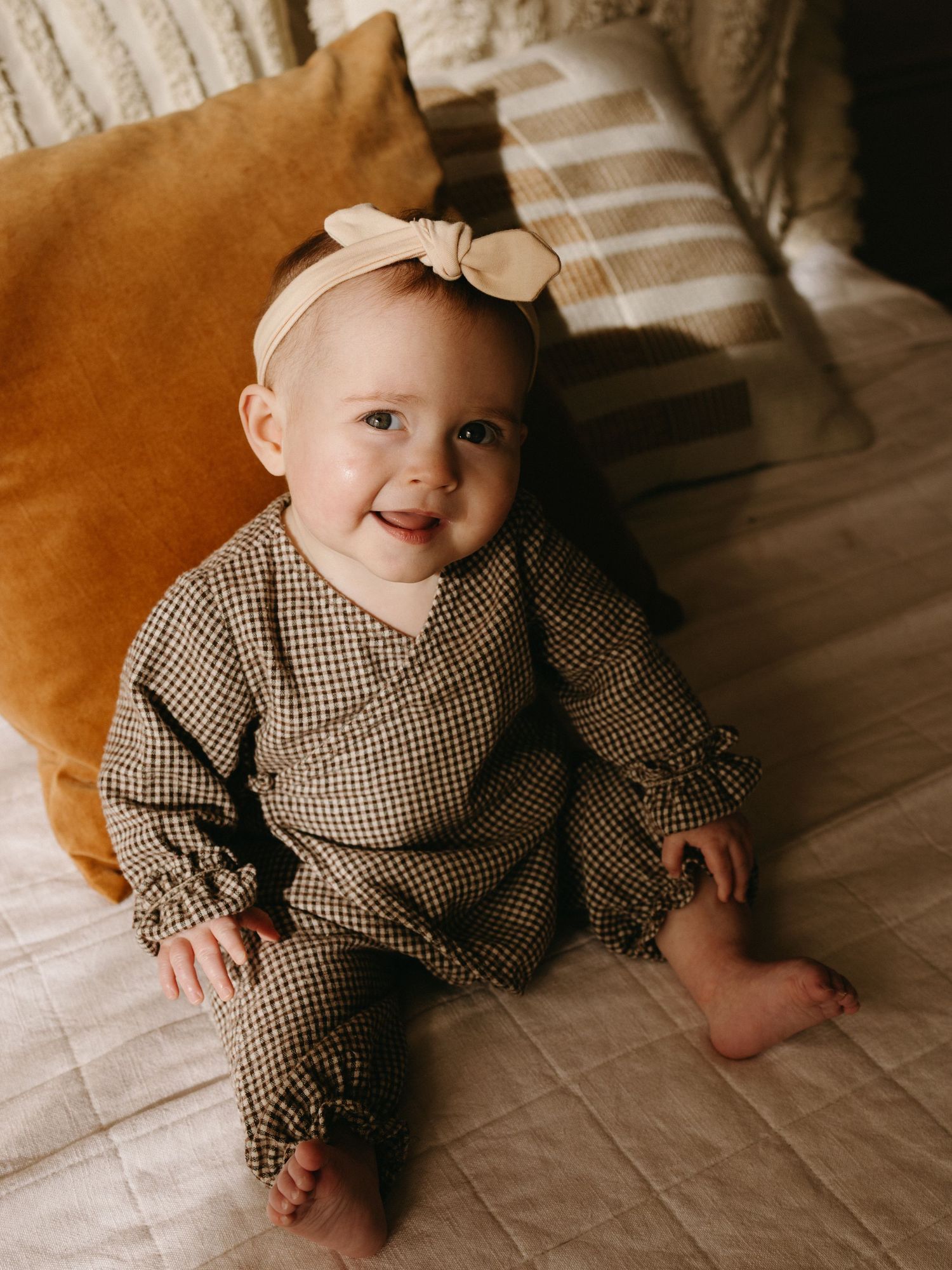 Baby wearing checkered outfit resting on brown couch cushions.