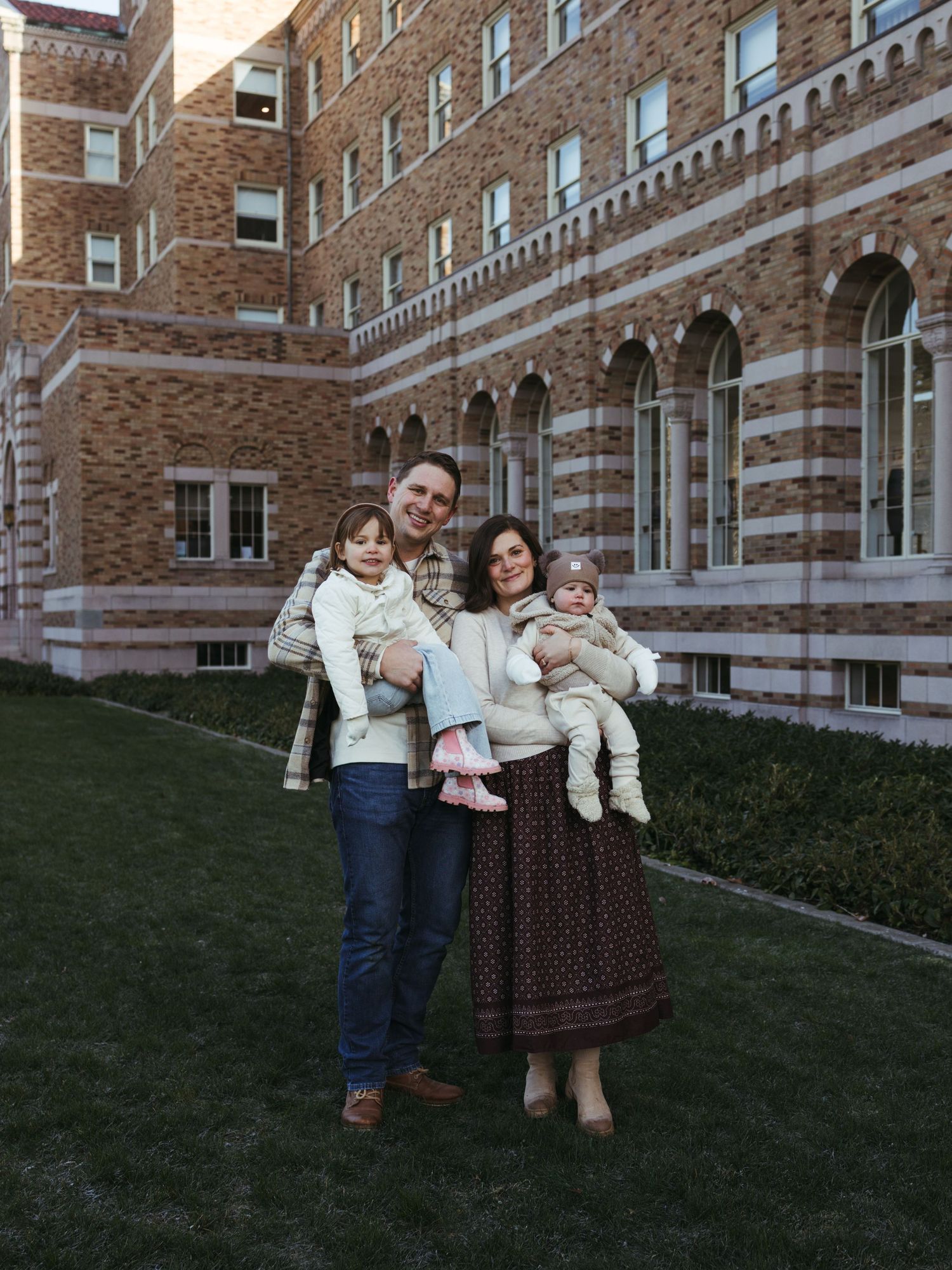 A family portrait taken outside a beautiful brick university building with arched windows.