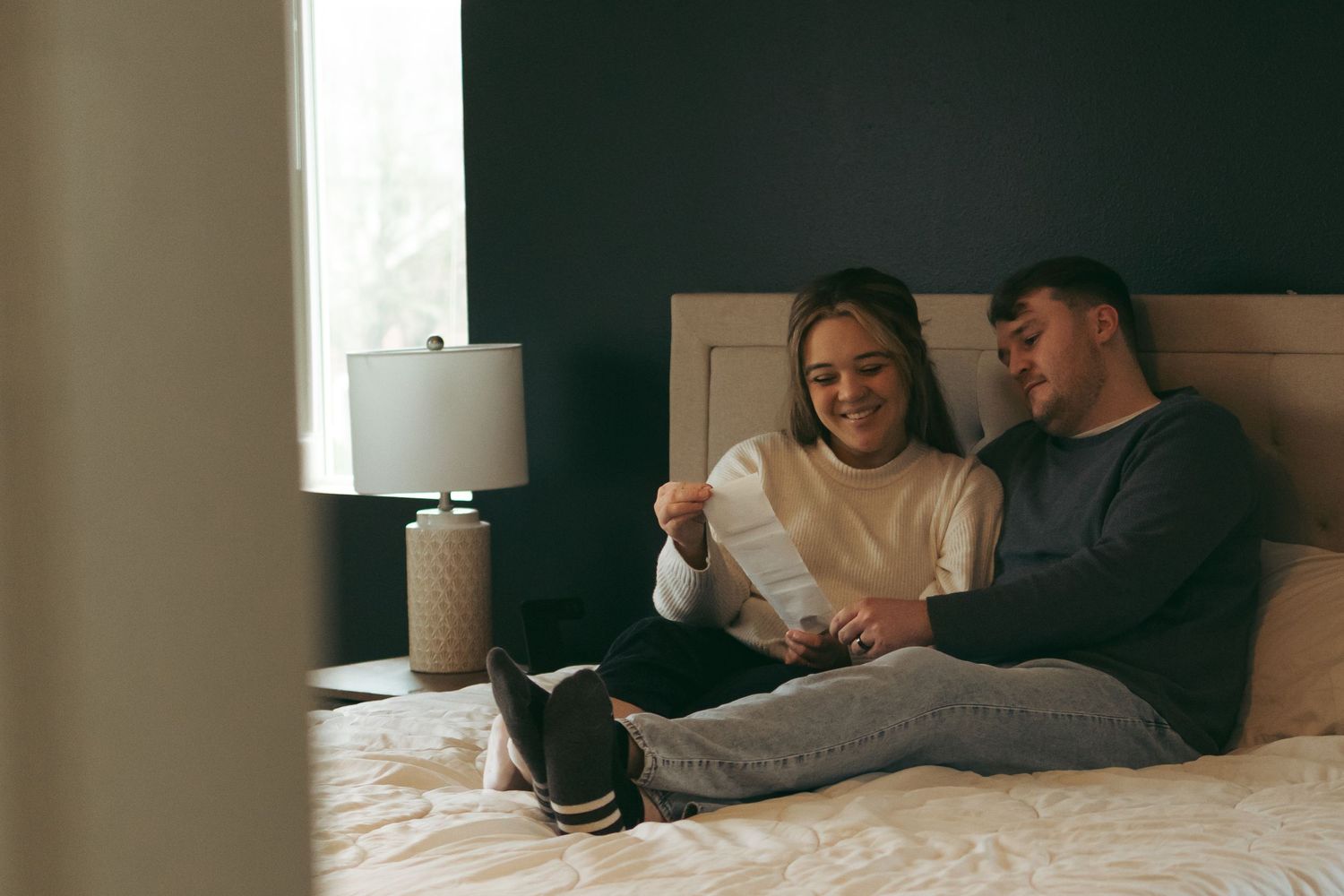 A couple relaxing together on bed while looking at something in their hands.