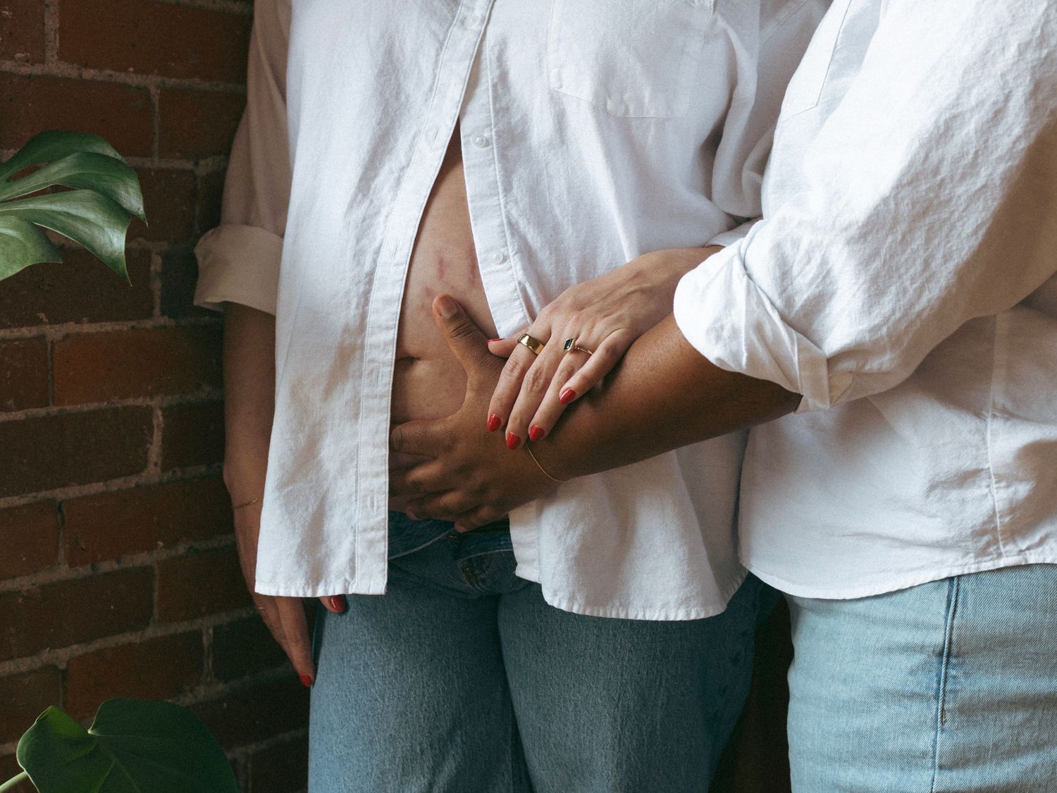 Candid moments captured pregnant belly  in white button-down shirts against an industrial brick wall setting.