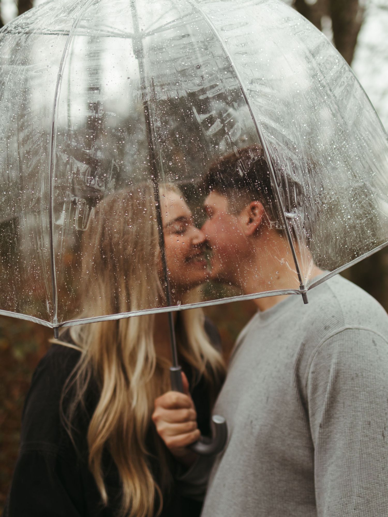 Couple sharing romantic moment under clear umbrella in the rain.