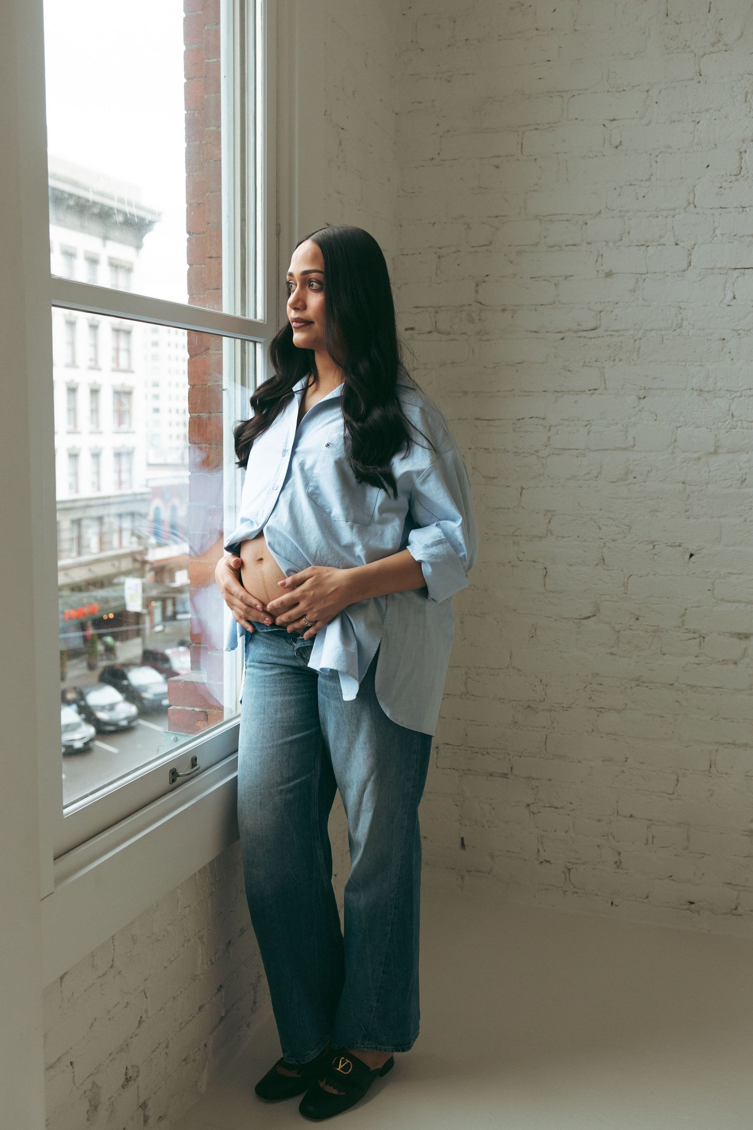 Casual lifestyle portraits of a woman by large windows in an urban studio space.
