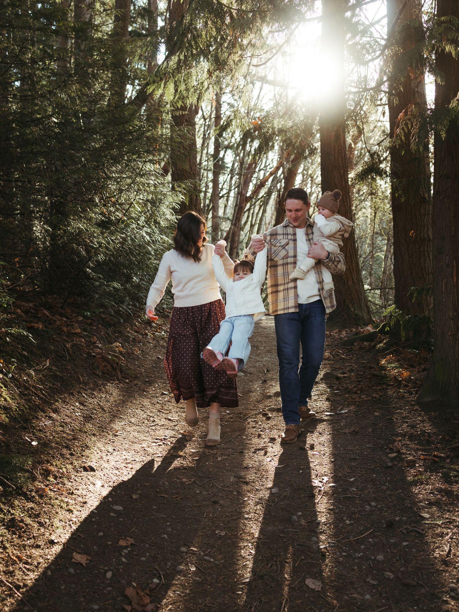 Silhouettes of people walking on a sunlit forest path among tall trees.