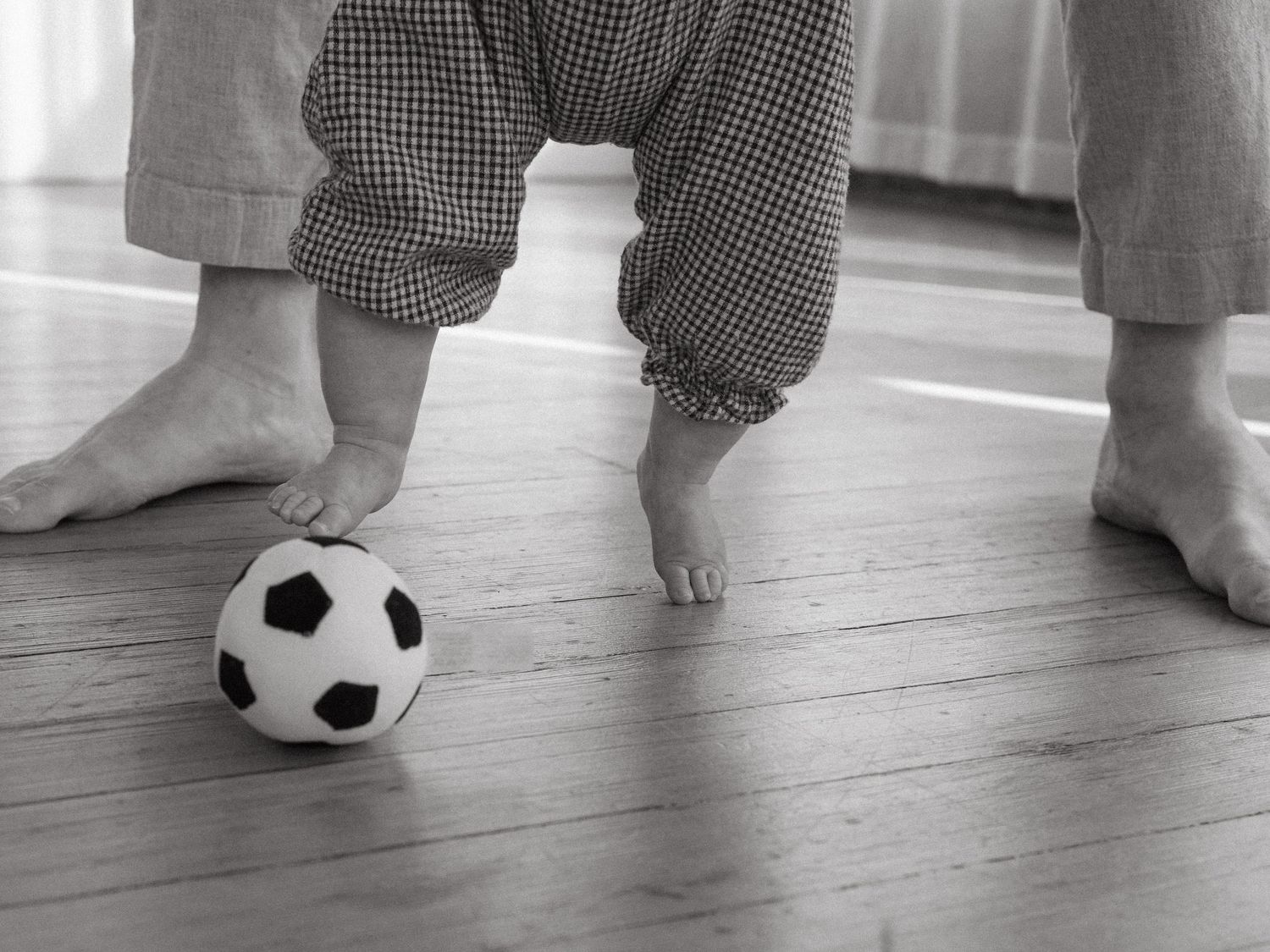 Close-up view of bare feet playing with a small soccer ball on a wooden floor.