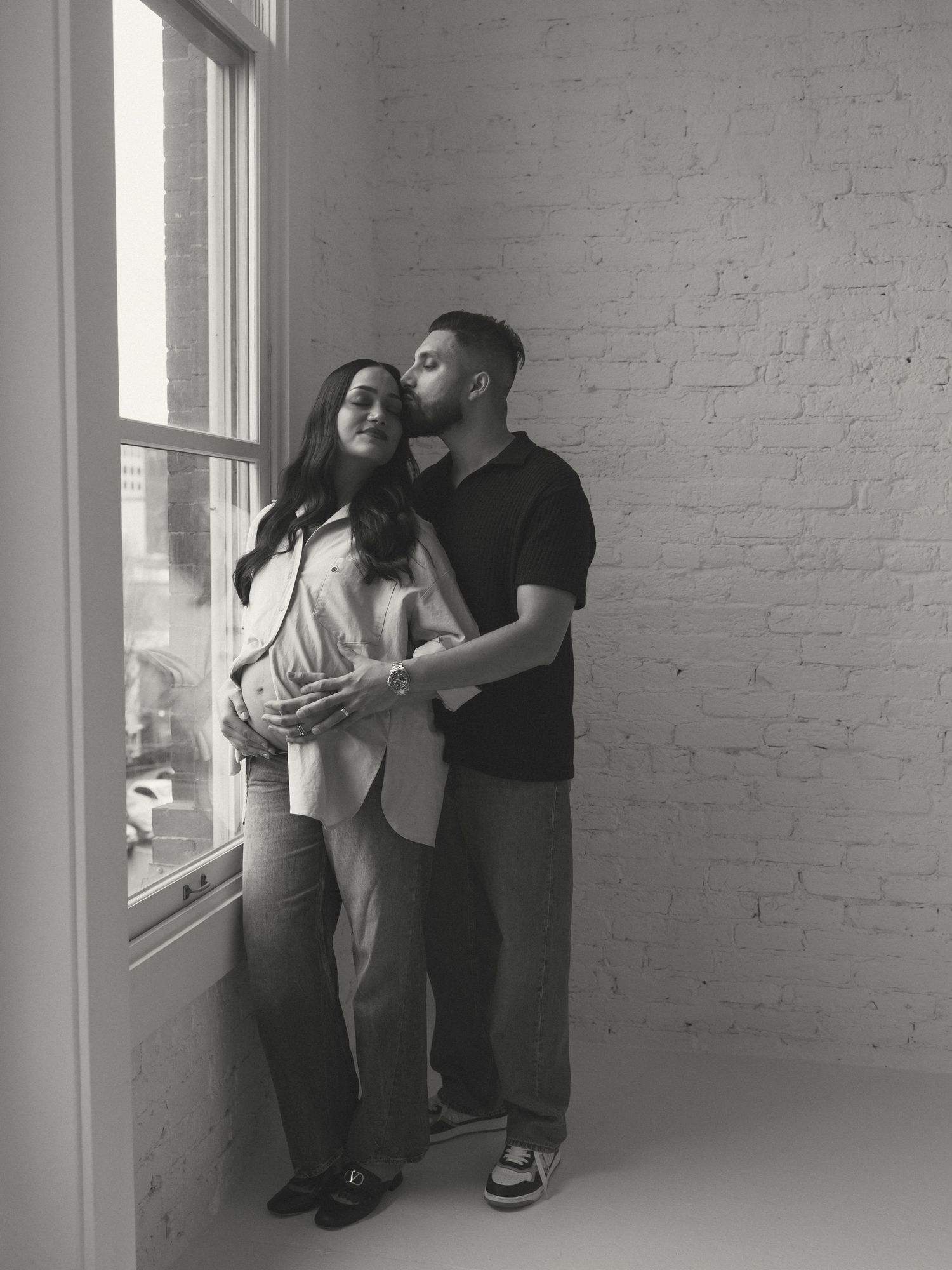 Intimate family moments captured in a bright minimalist studio with white brick walls.