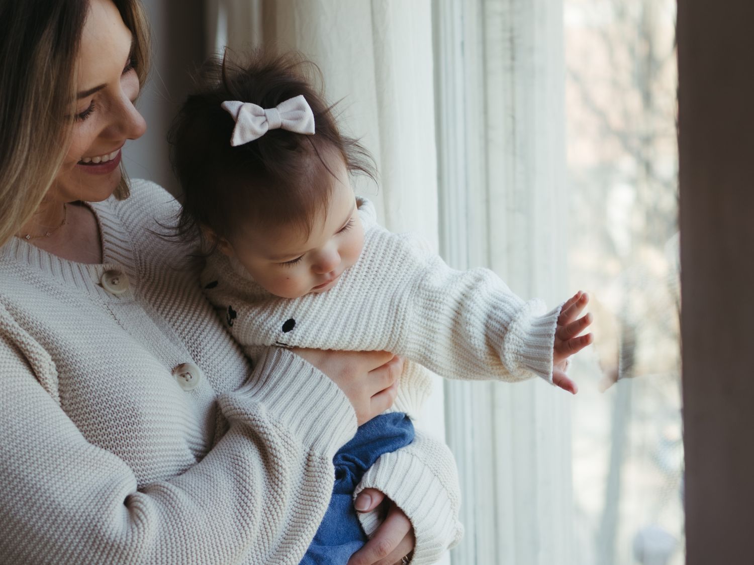 A heartwarming moment by the window as a child in white reaches out while being held.