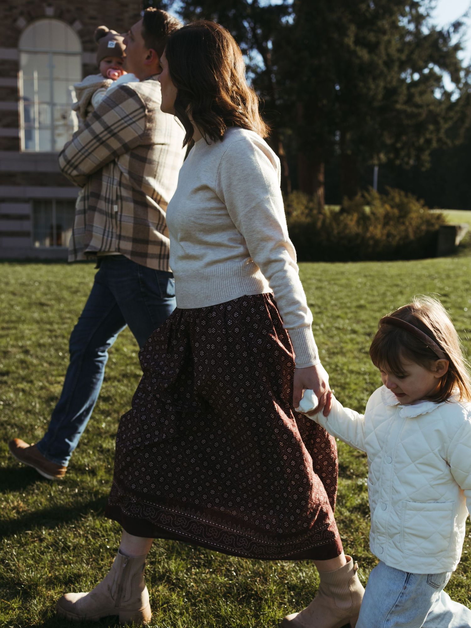 A family walks together on grass with historic buildings in the background.