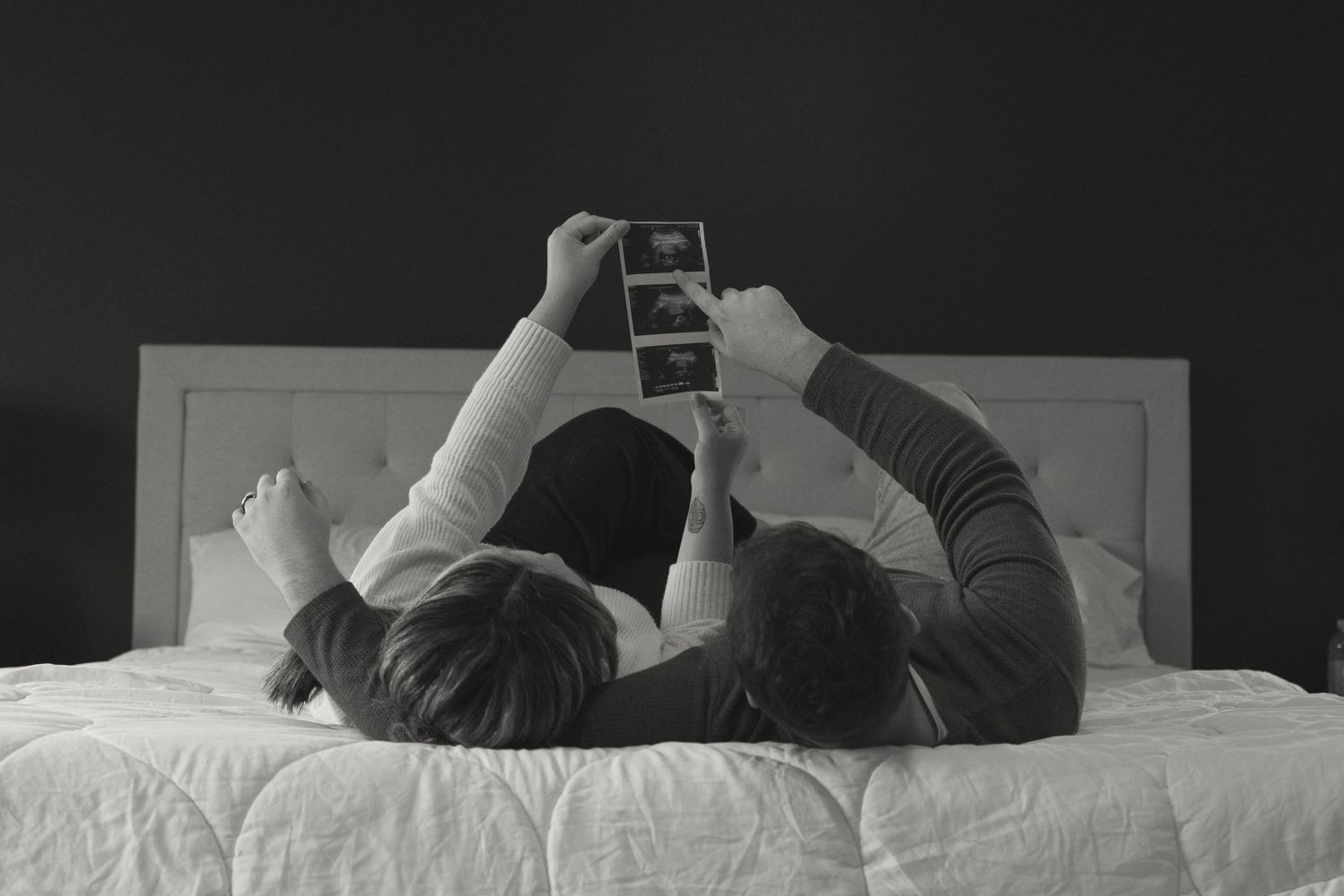A couple lying on bed looking at something on their phone together.