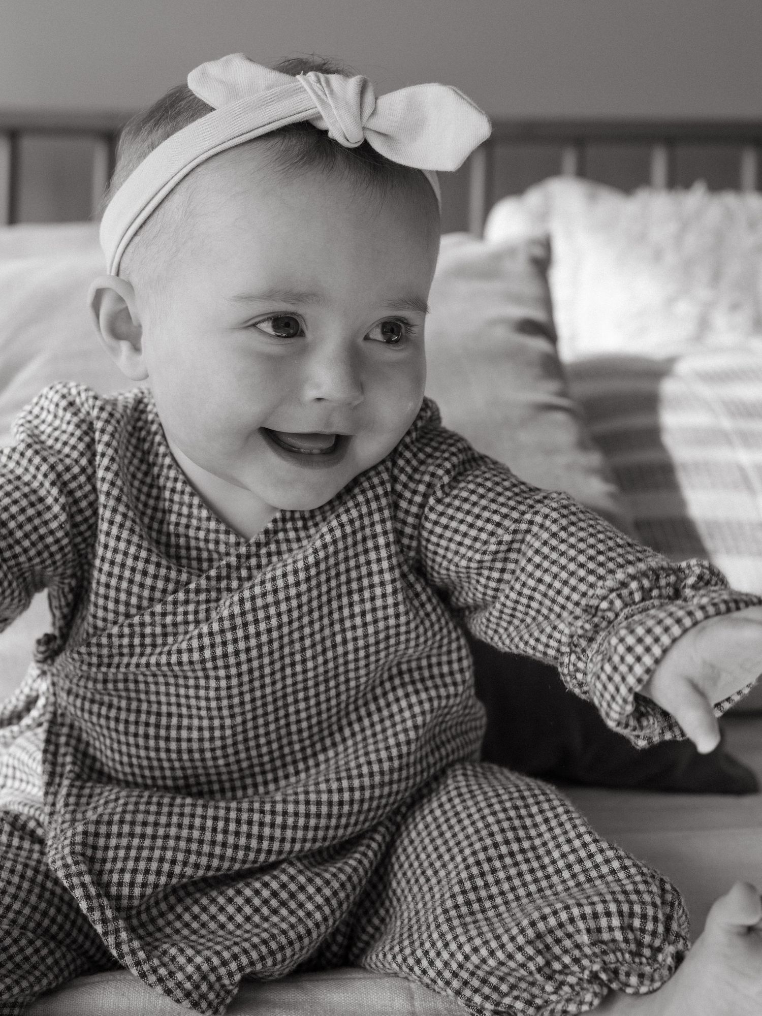 Black and white photo of a baby in gingham outfit lying down and smiling.