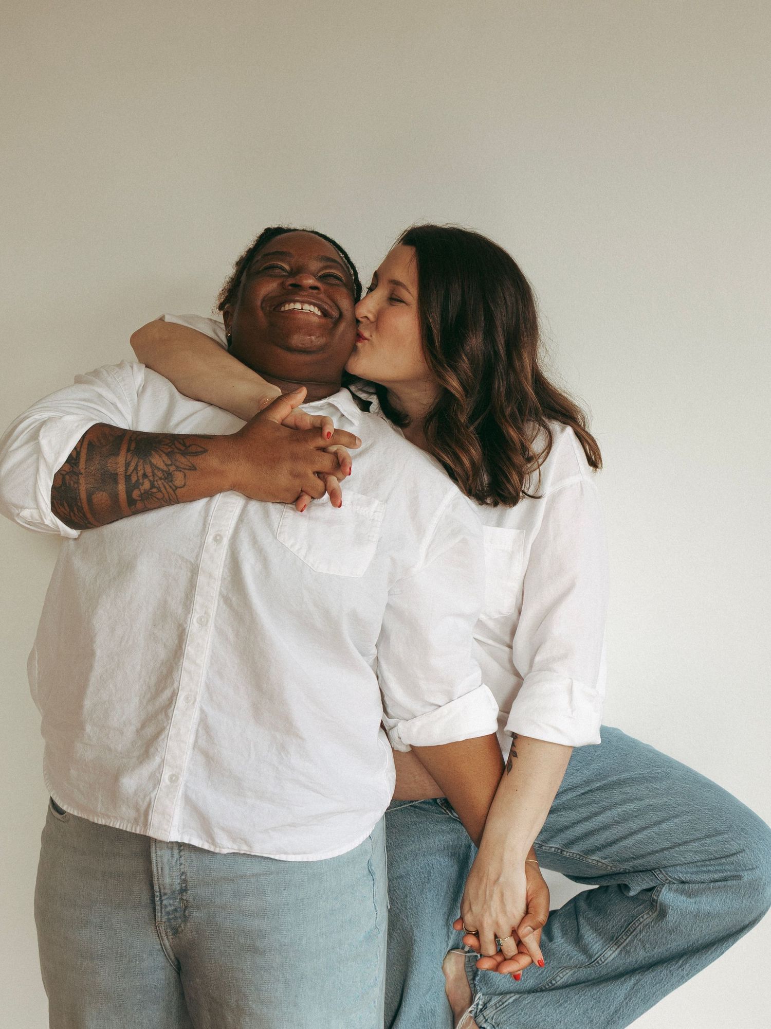 Two people in white shirts and jeans share candid laughing moments on hardwood floor.