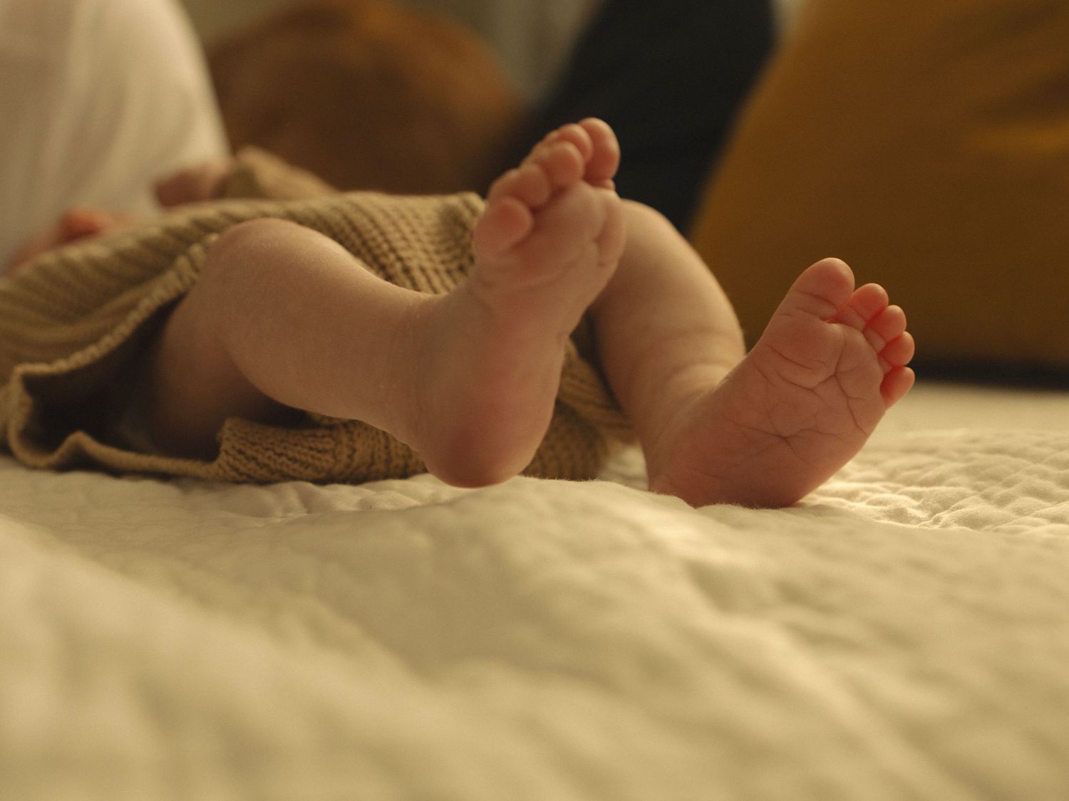 Detail shots of baby's tiny feet and legs in warm indoor lighting.