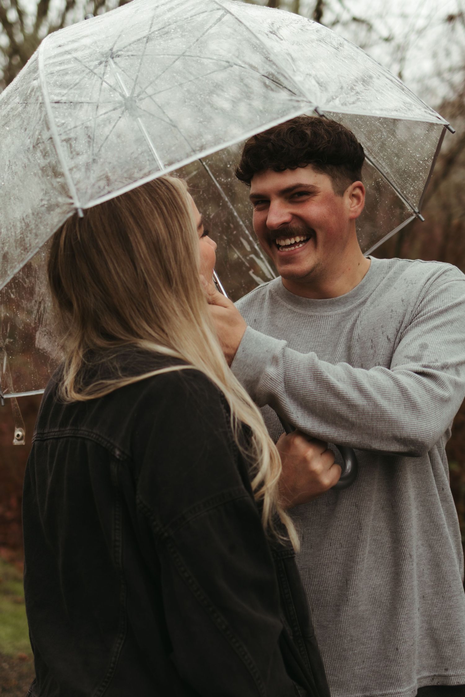 Couple laughing together under transparent umbrella during autumn photoshoot.