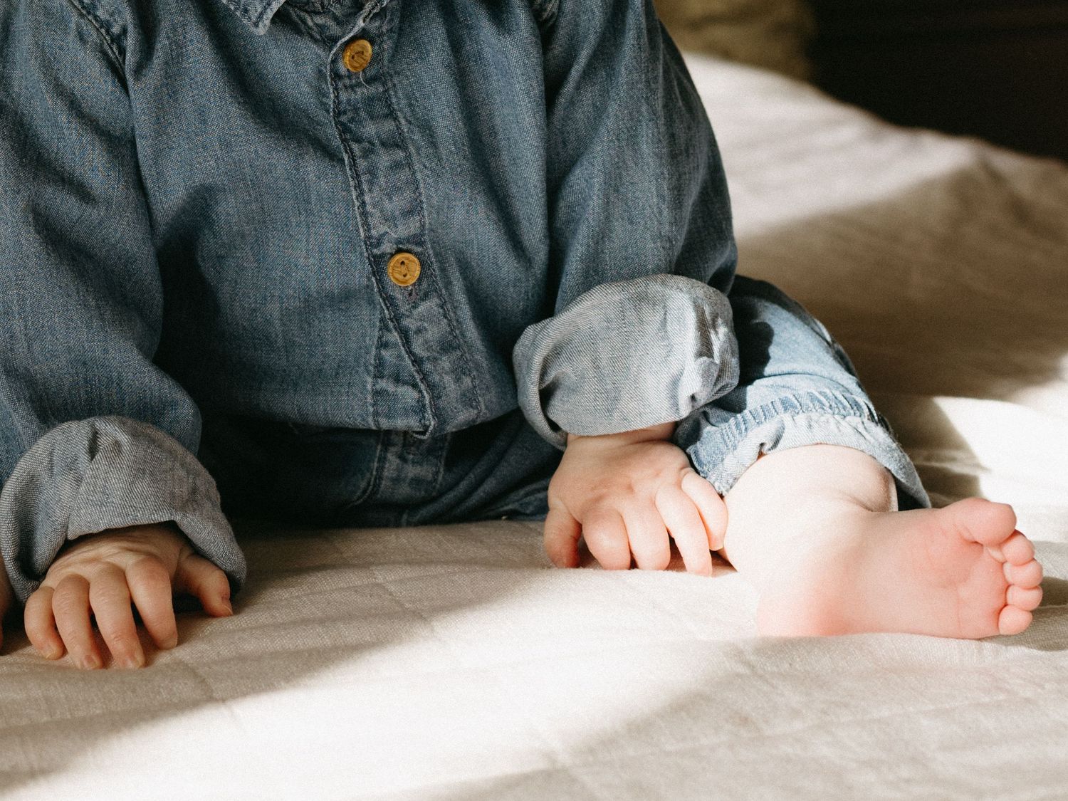 Close-up of tiny feet and hands against white bedding.