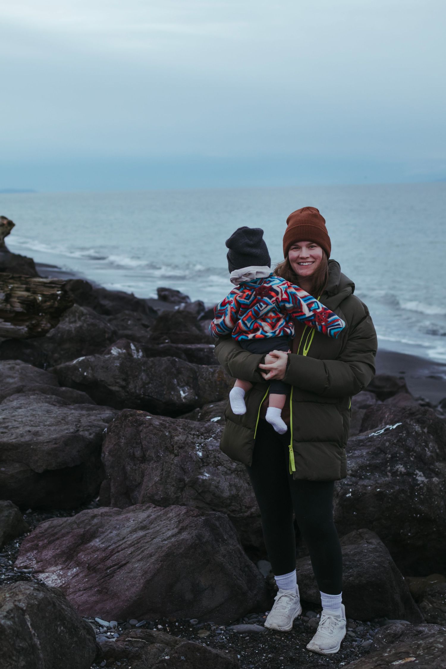 Family enjoying time together on rocky coastal shoreline during overcast day.