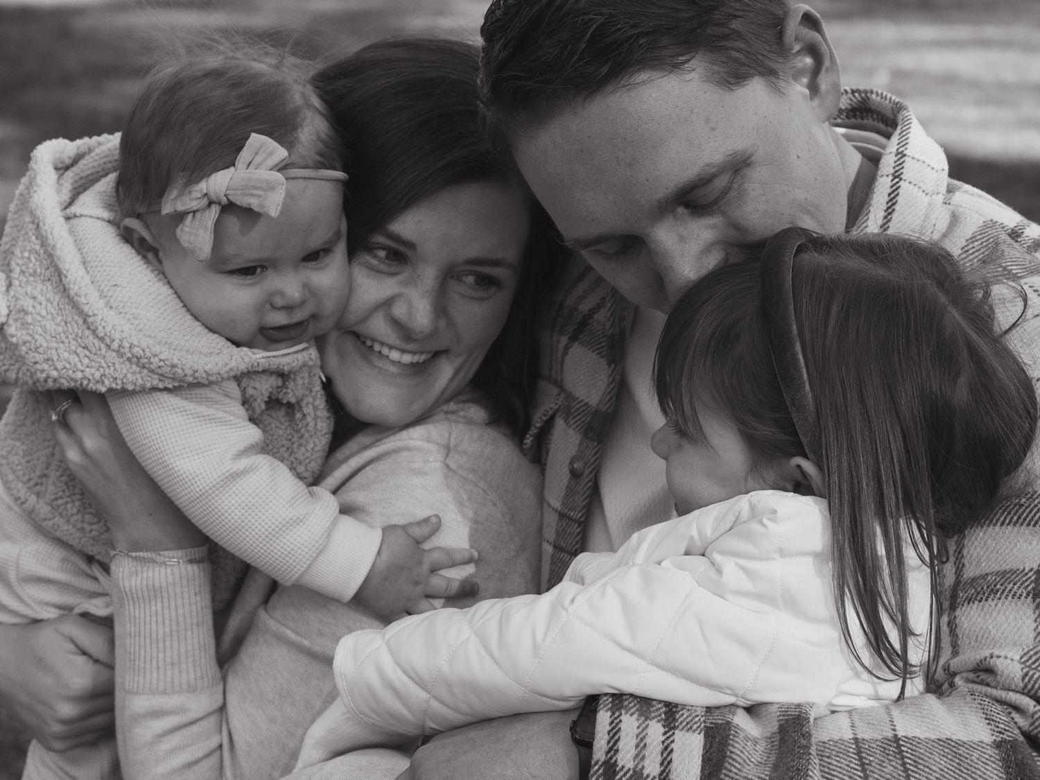 Intimate black and white portrait of people embracing on a blanket outdoors.