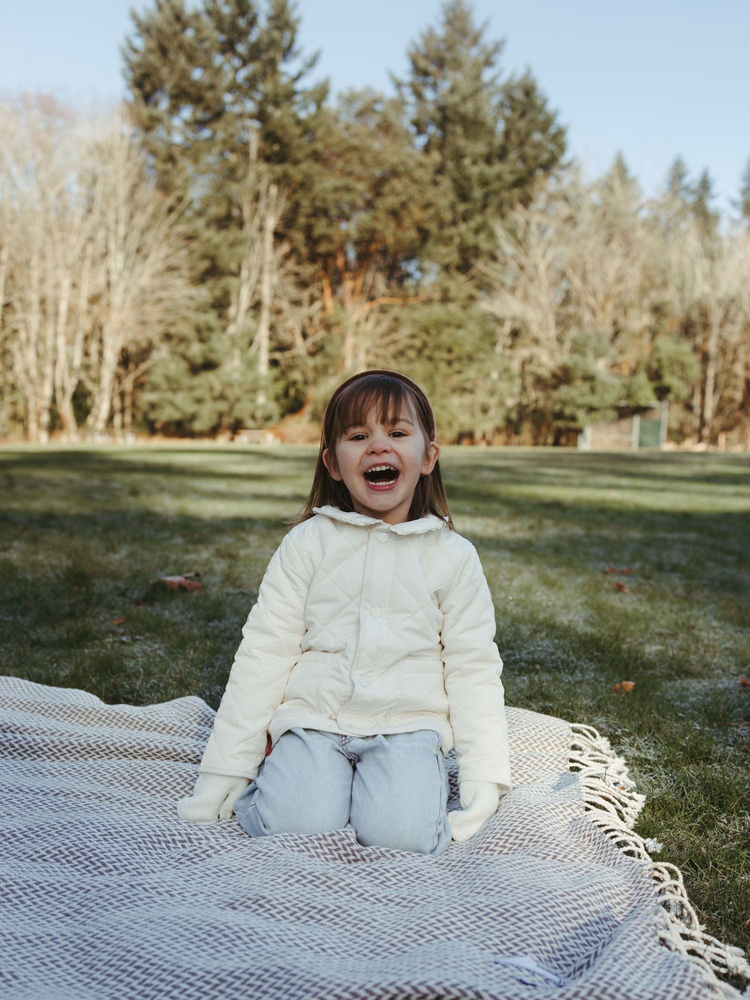 A child sits on a blanket outdoors laughing with pure joy.